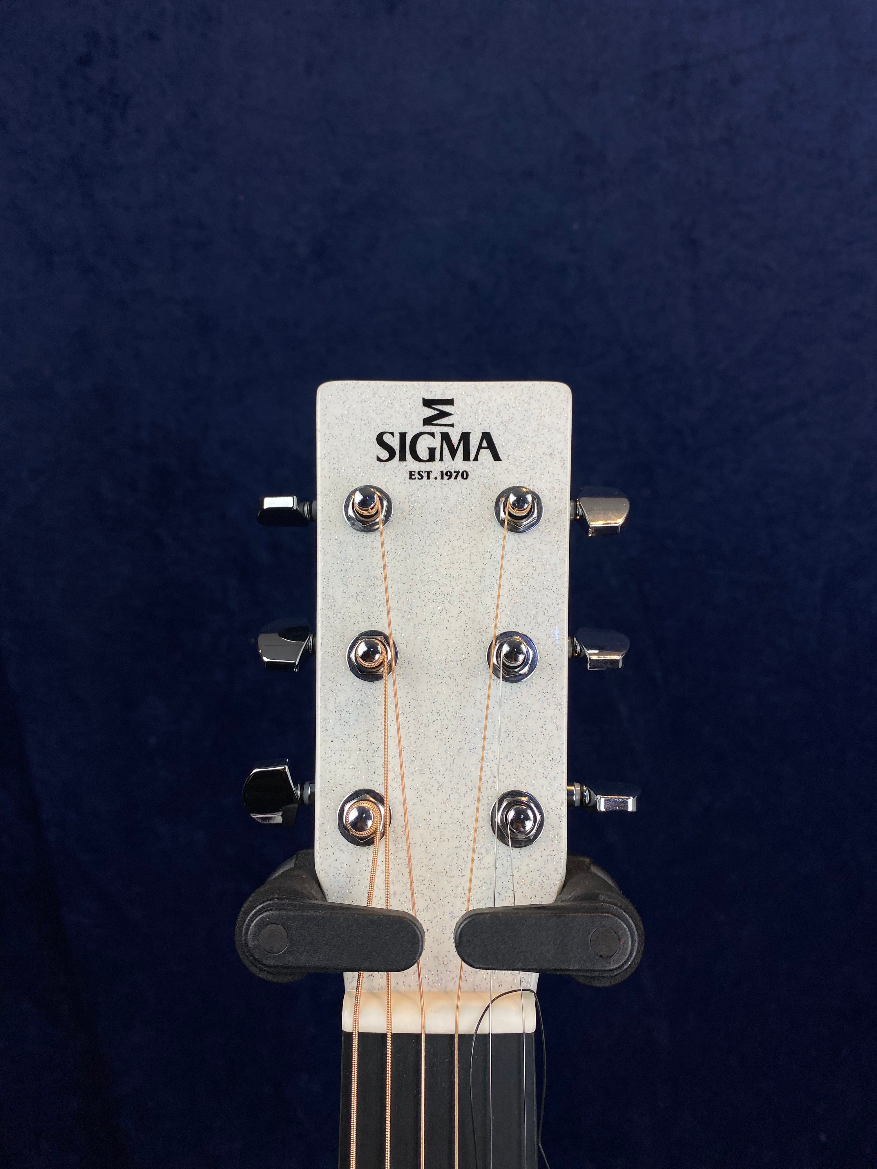 The headstock of a Sigma acoustic guitar shows six tuning pegs, with "SIGMA EST. 1970" printed on the front in black letters.