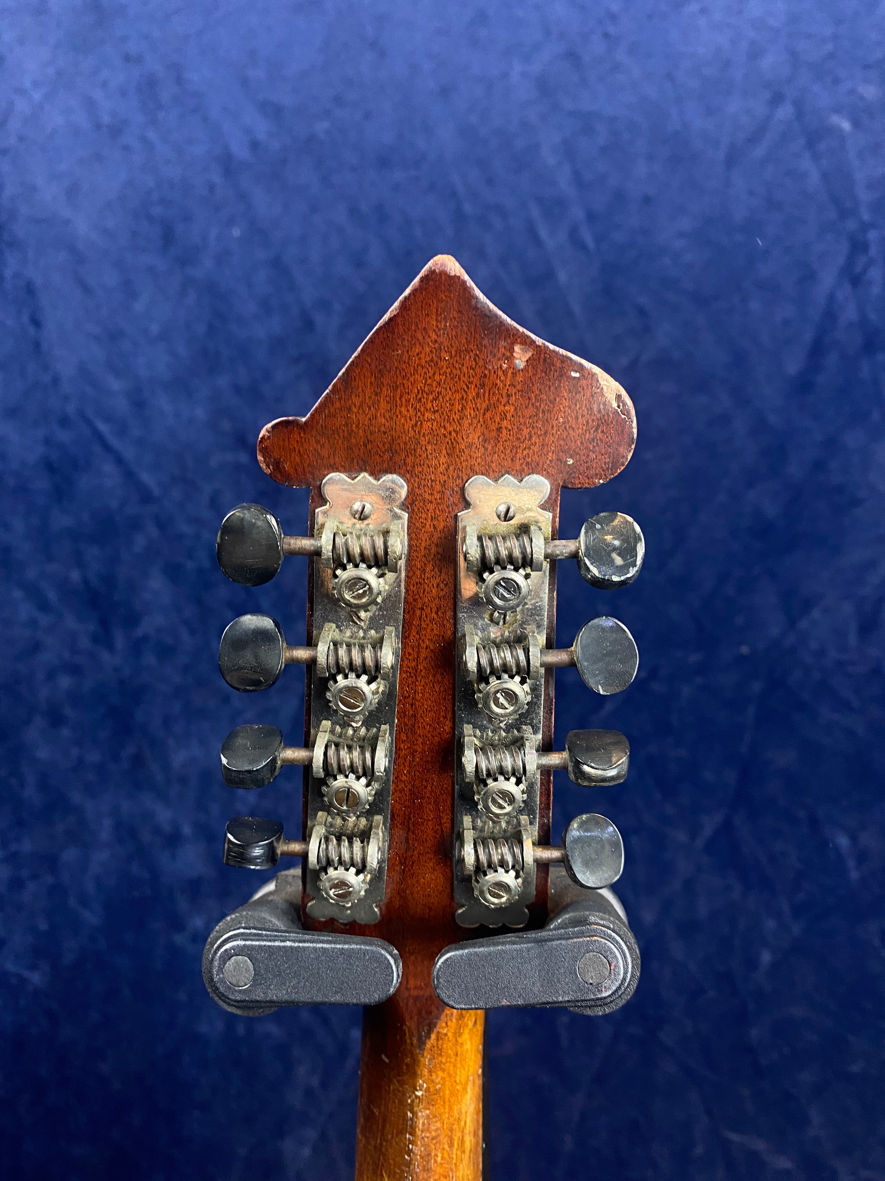 Eight metal tuning pegs and gears on the back of a wooden mandolin headstock, set against a dark blue textured background.