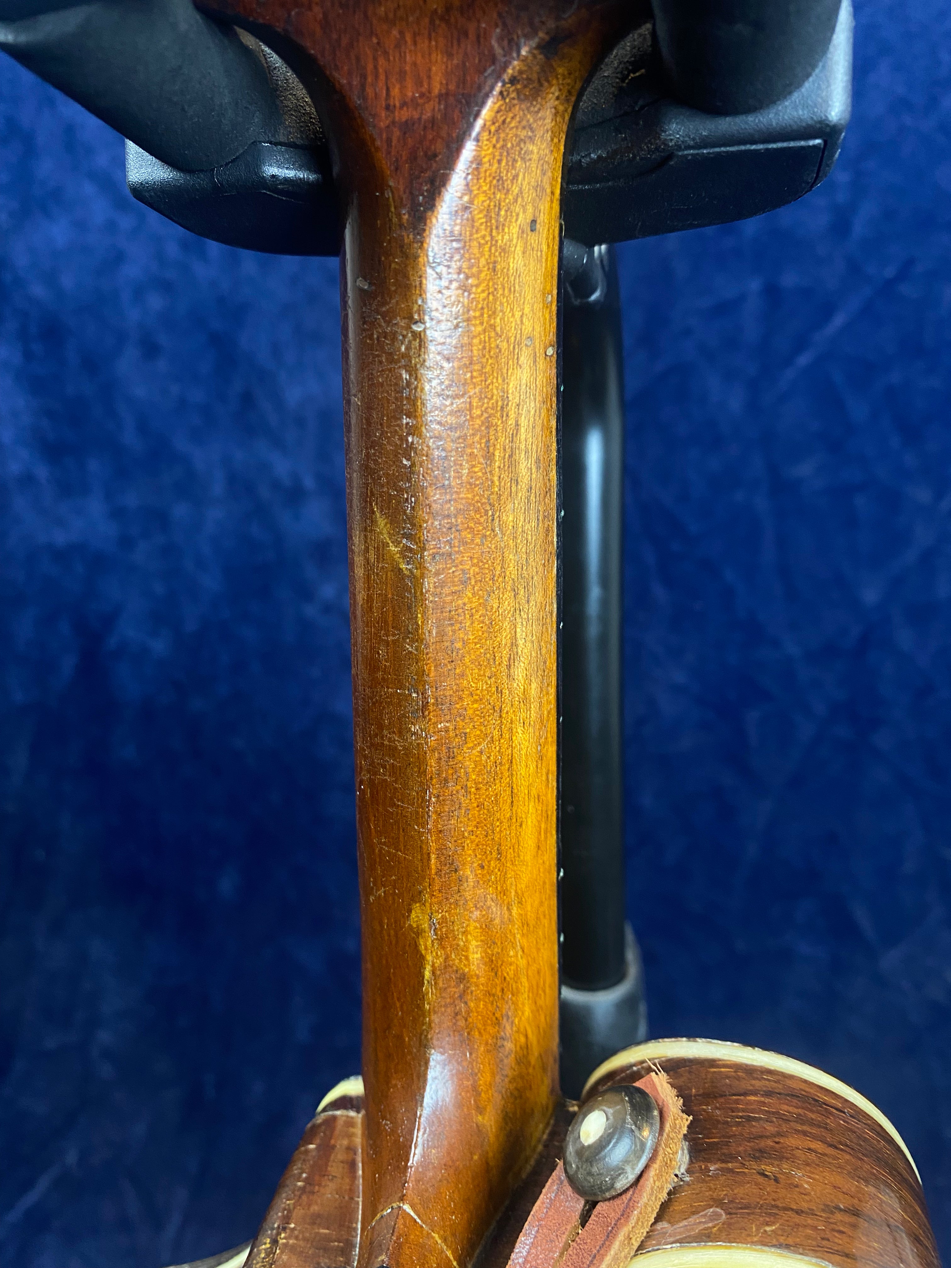 Close-up of a mandolin neck with visible wood grain, light scratches, and minor wear; part of the instrument's body and strap button shown.