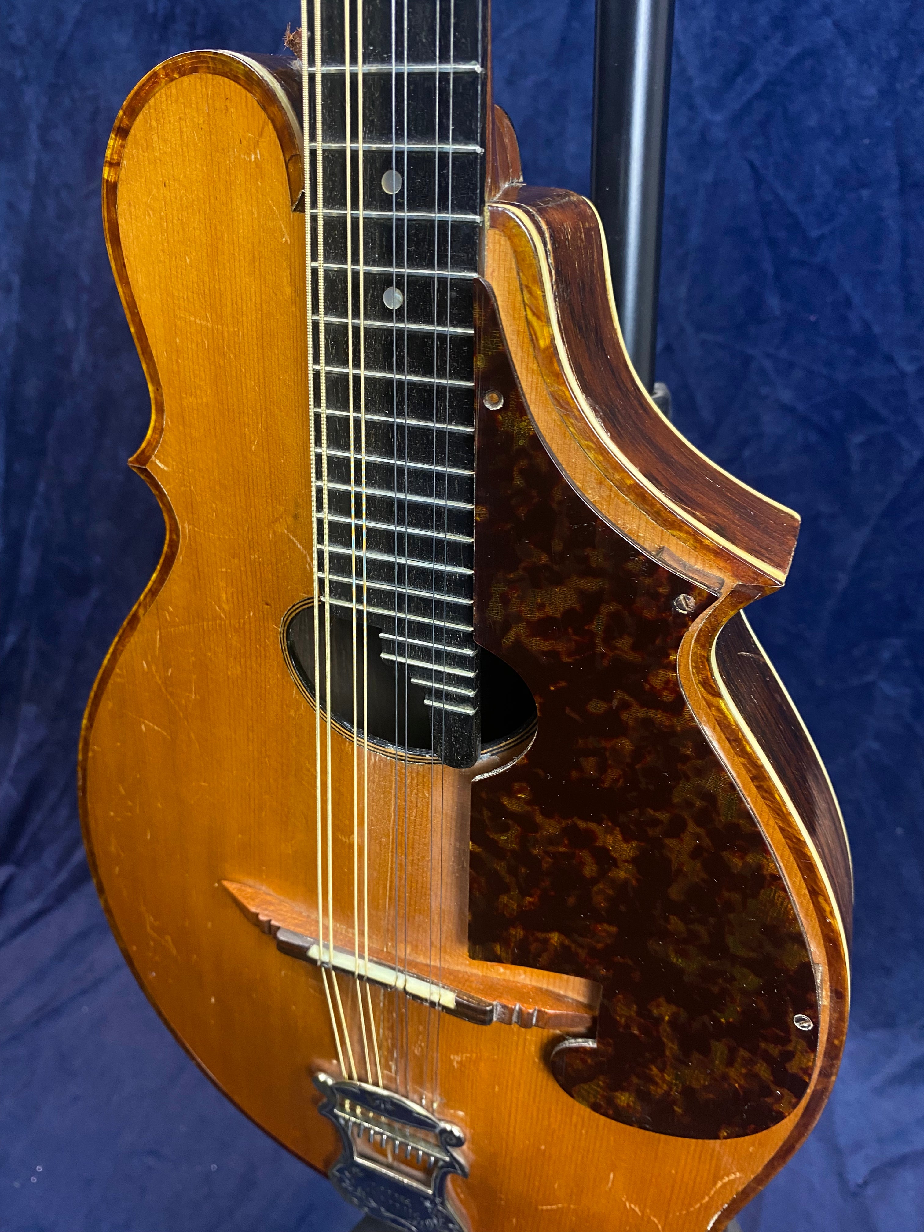 Wooden mandolin with a tortoiseshell-patterned pickguard, eight strings, and a carved bridge. The finish shows wear, giving it a vintage look.