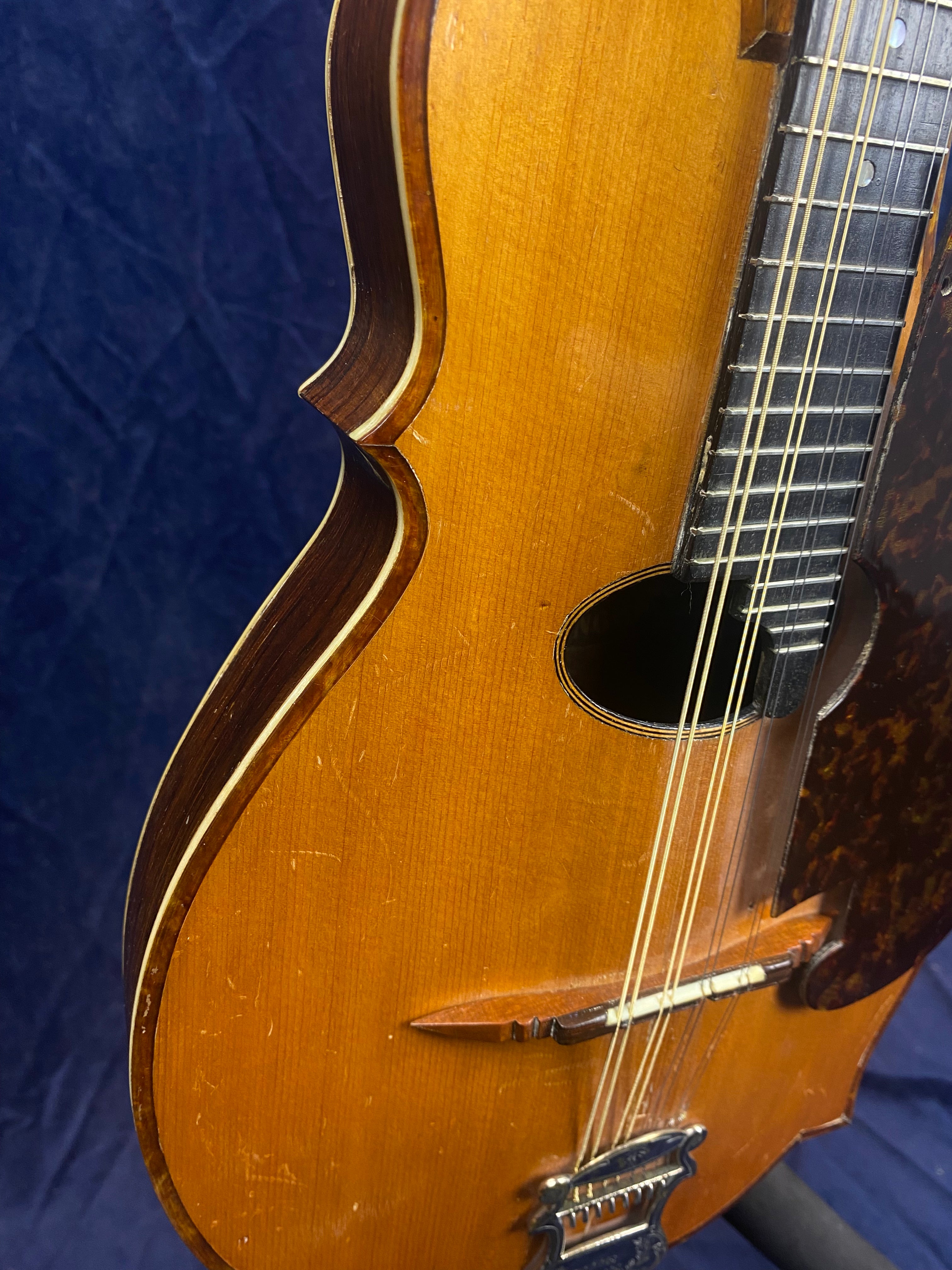 Close-up of a wooden mandolin body showing its strings, bridge, pickguard, and contoured edges against a dark background.