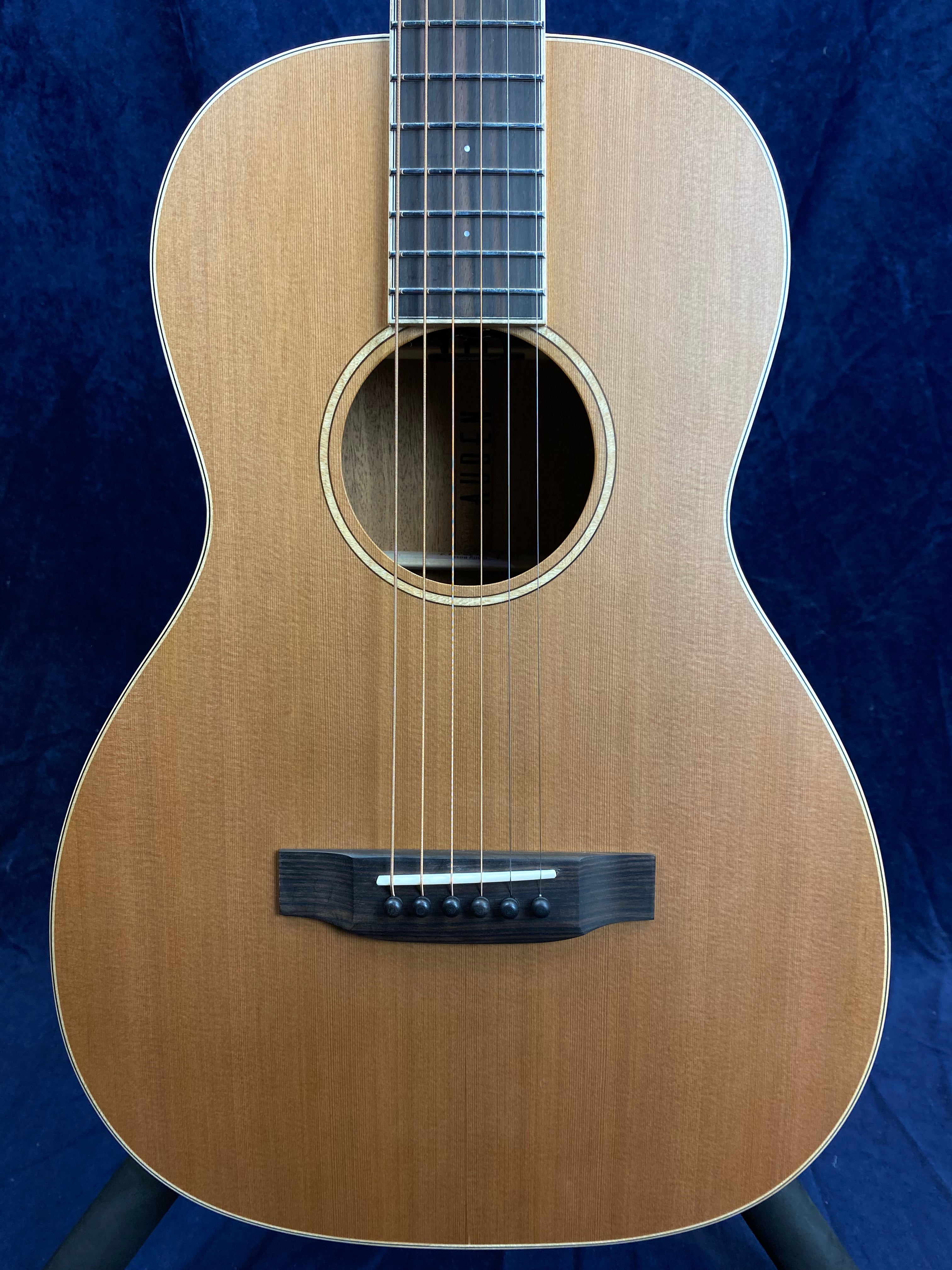 Natural wood acoustic guitar body with six strings, a circular sound hole, dark wooden bridge, and light-colored trim against a dark blue background.