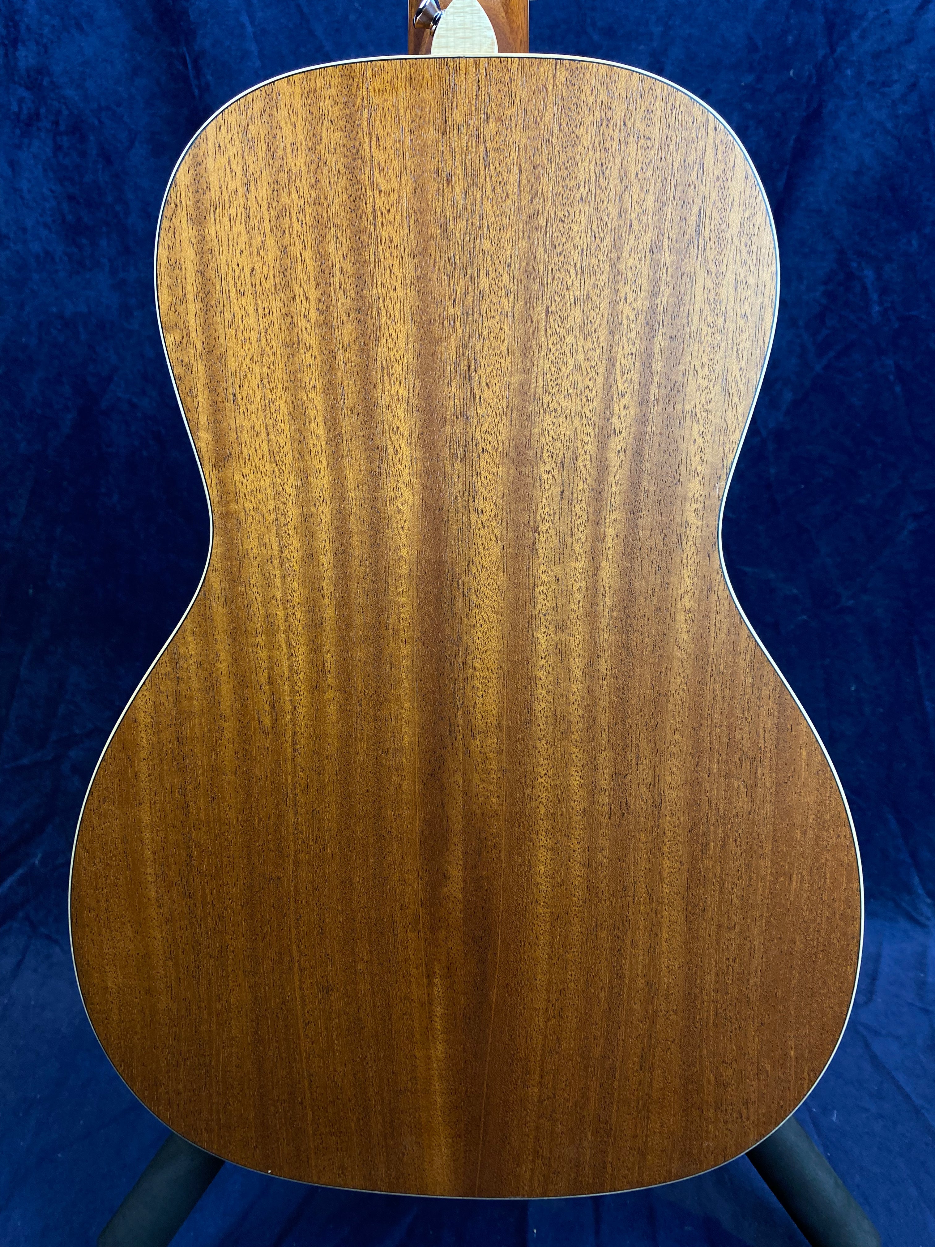 The back of an acoustic guitar, showing smooth brown wood grain with light trim along the edges against a dark blue background.