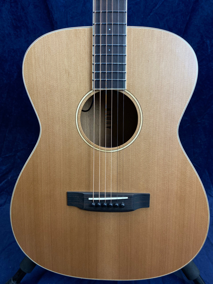 Natural wood acoustic guitar with a round sound hole, six strings, and a dark bridge, displayed upright against a dark blue background.