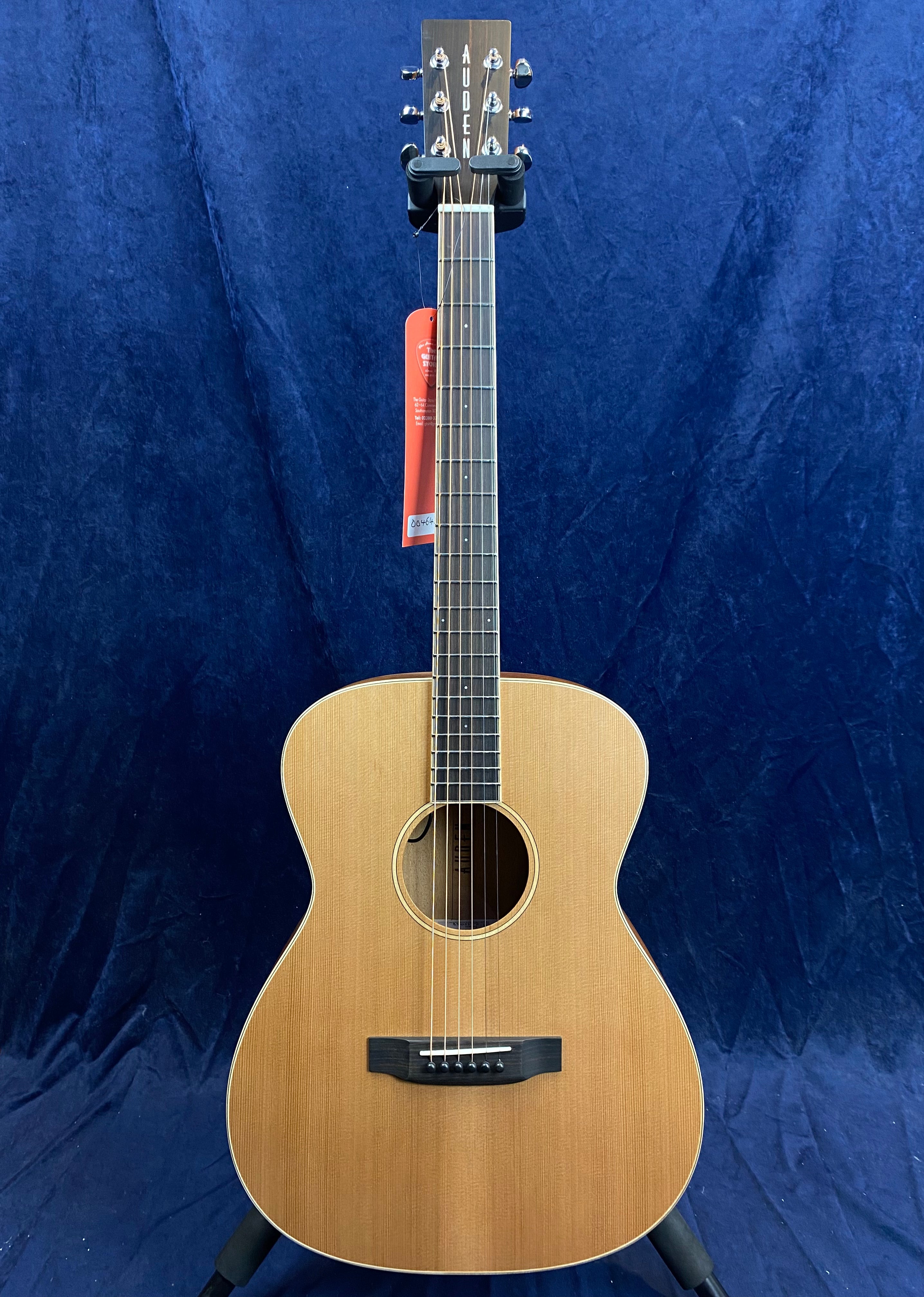 Light wood acoustic guitar with six strings, rounded body, dark wood fretboard, and “Auden” on the headstock, set against a deep blue background.