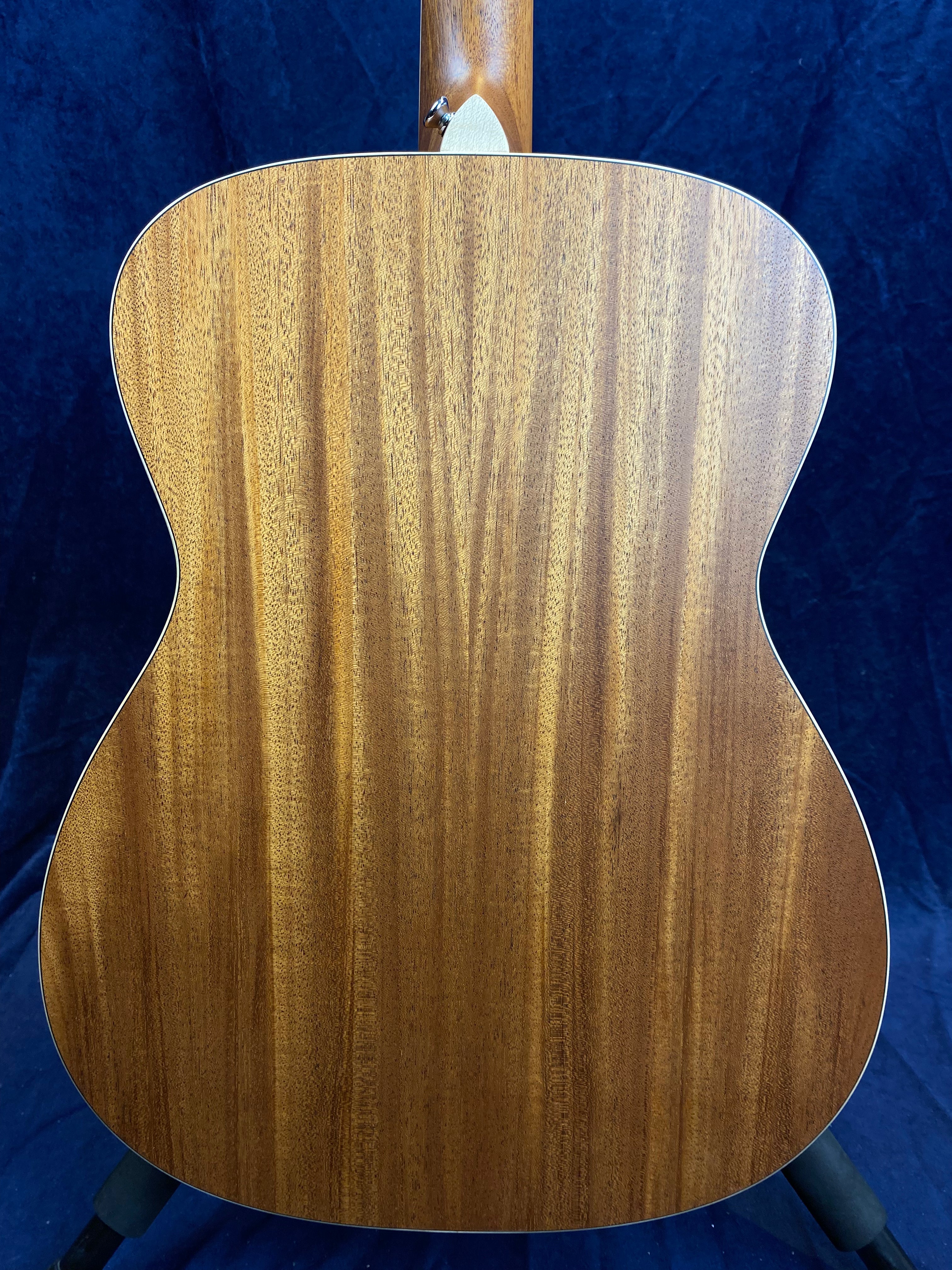 Back of an acoustic guitar made from smooth, medium-brown wood with vertical grain patterns, set against a dark blue background.