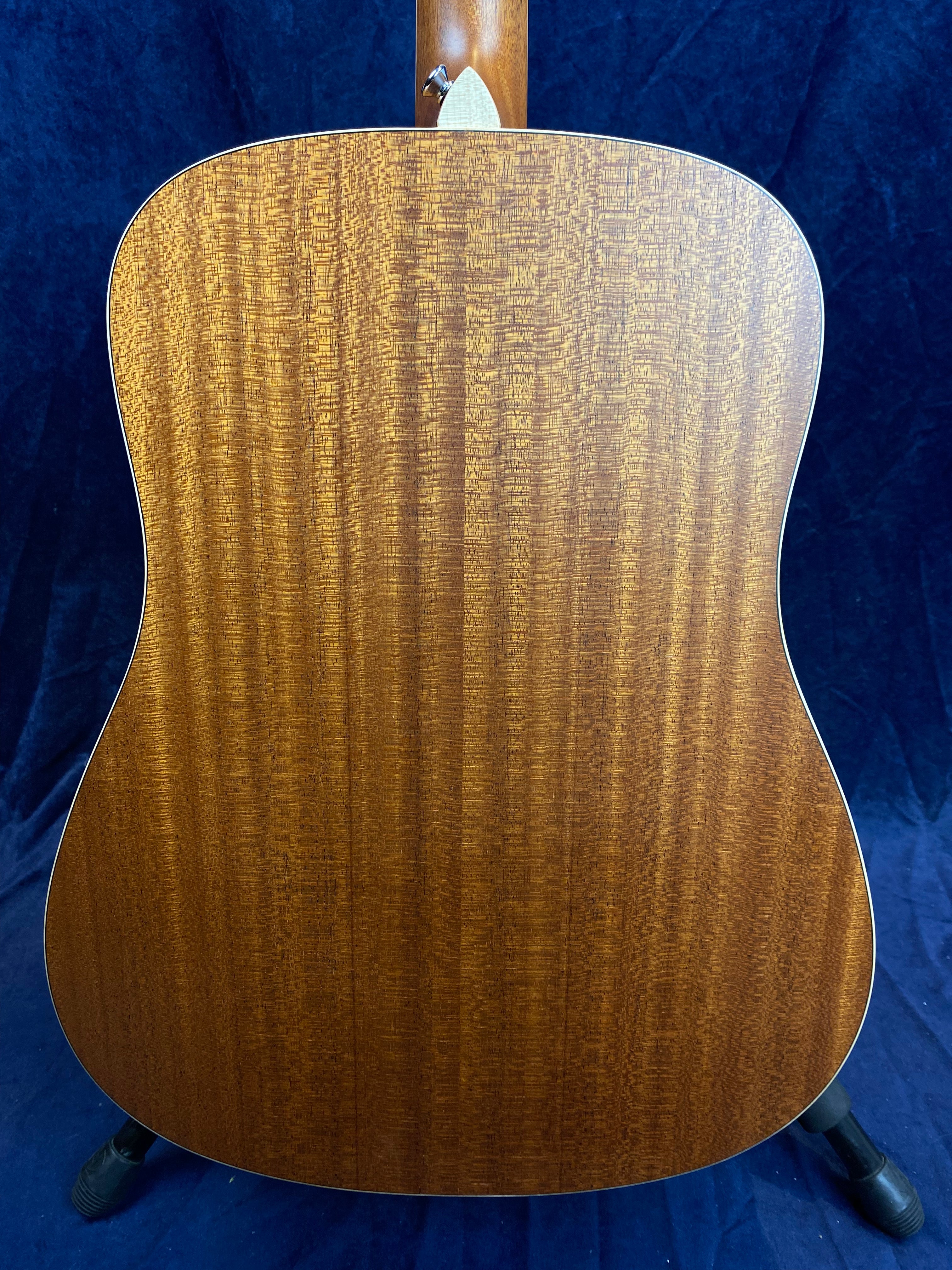 Back of an acoustic guitar showing rich, golden-brown wood with a prominent wavy grain pattern and light trim along the edges.