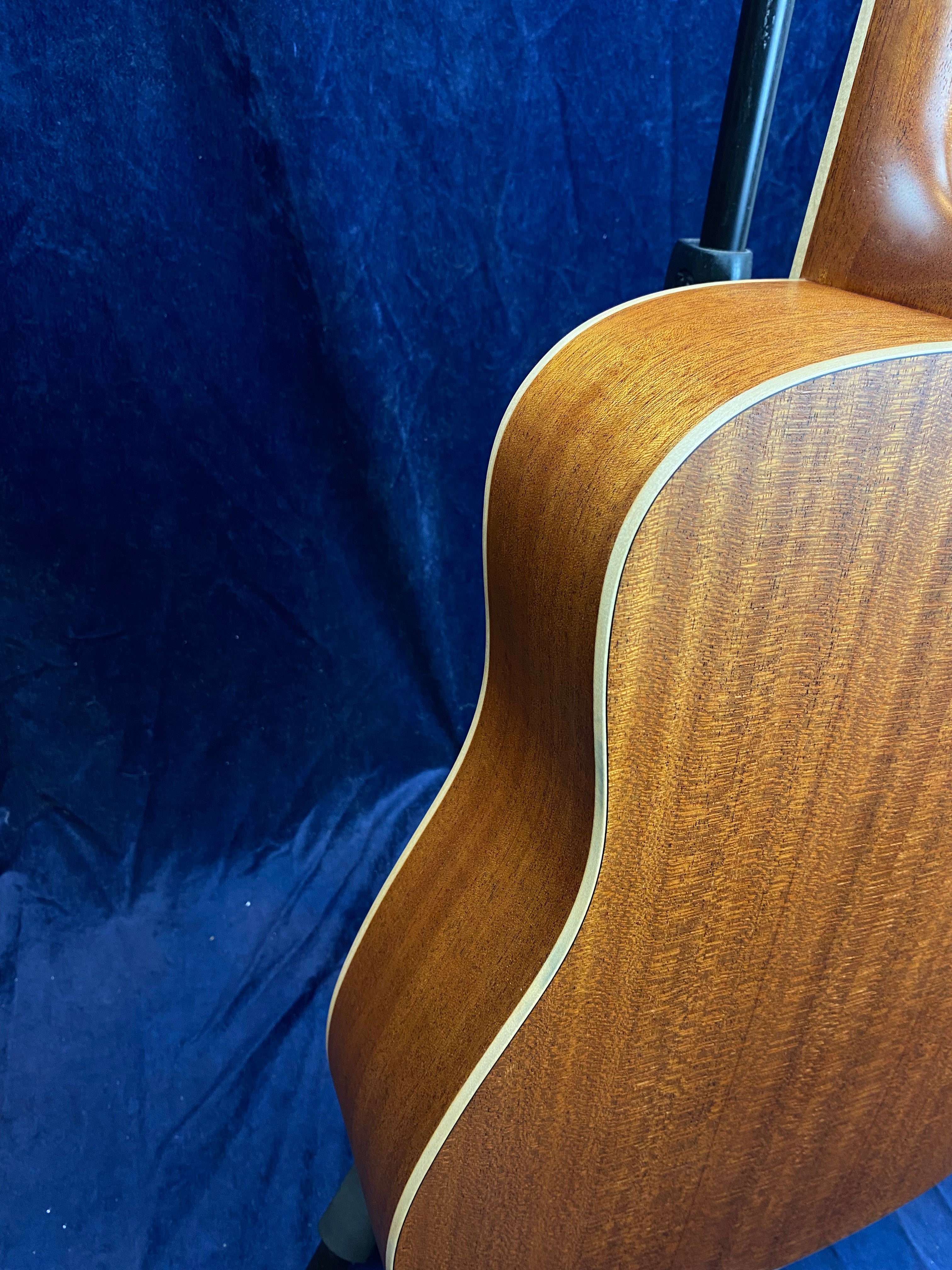 Curved side and back of a brown acoustic guitar with light wood binding, set against a dark blue textured background.