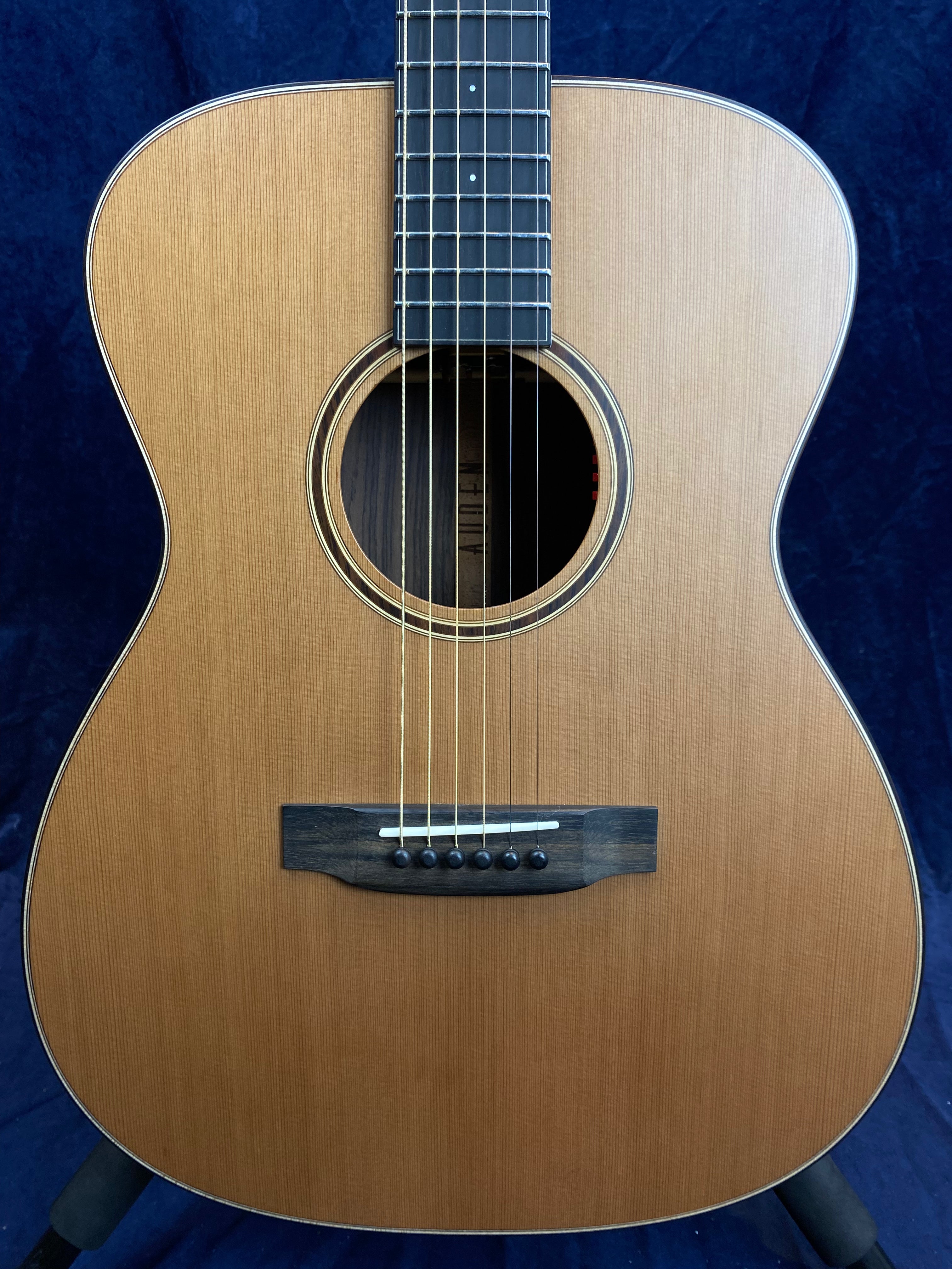 Steel-string acoustic guitar with a natural wood finish, round sound hole, black bridge, six bridge pins, and dark fretboard against a dark background.