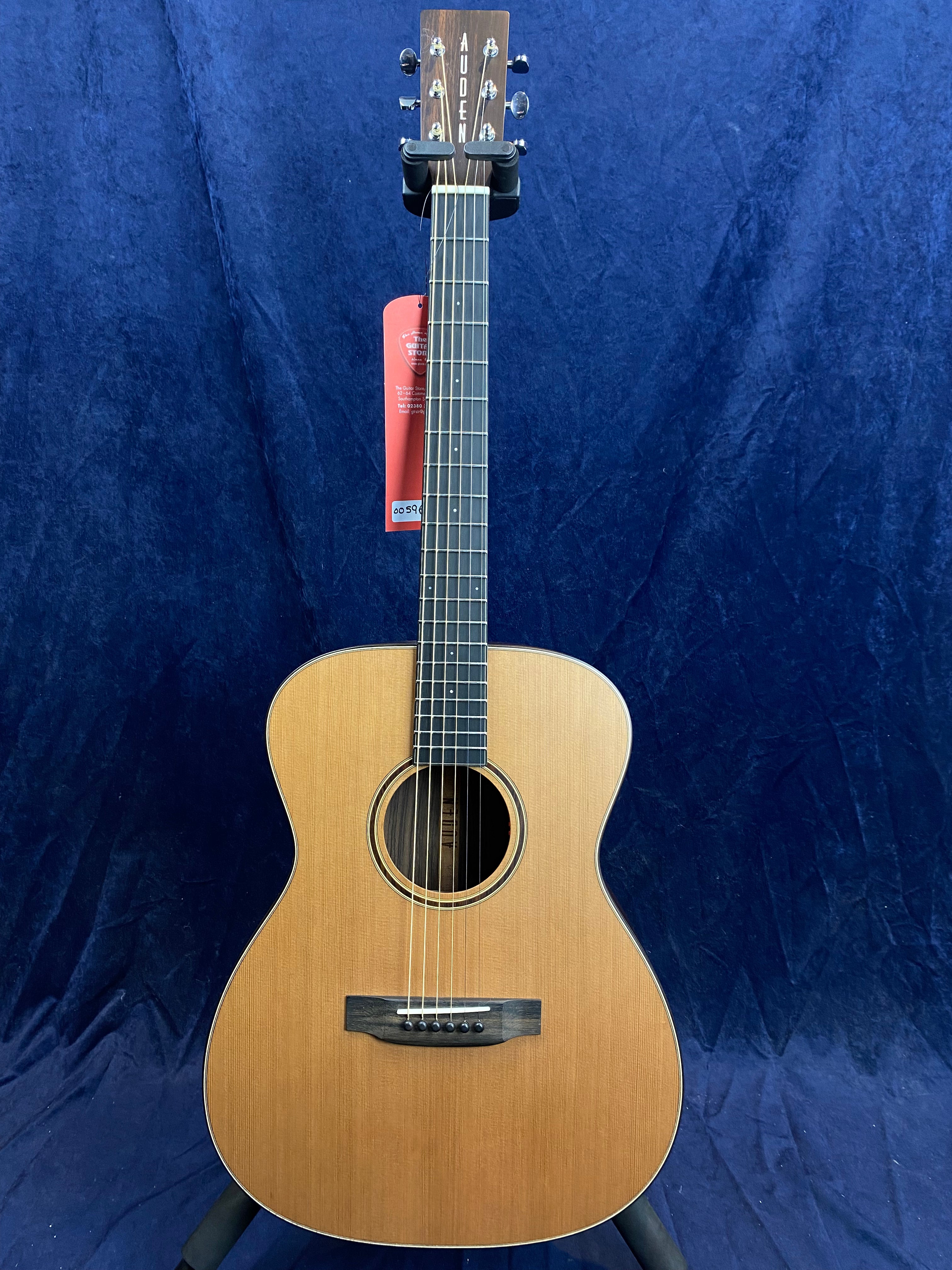 Light brown Auden acoustic guitar with a dark neck and headstock, chrome tuning pegs, and a red tag hanging from the top tuning post.