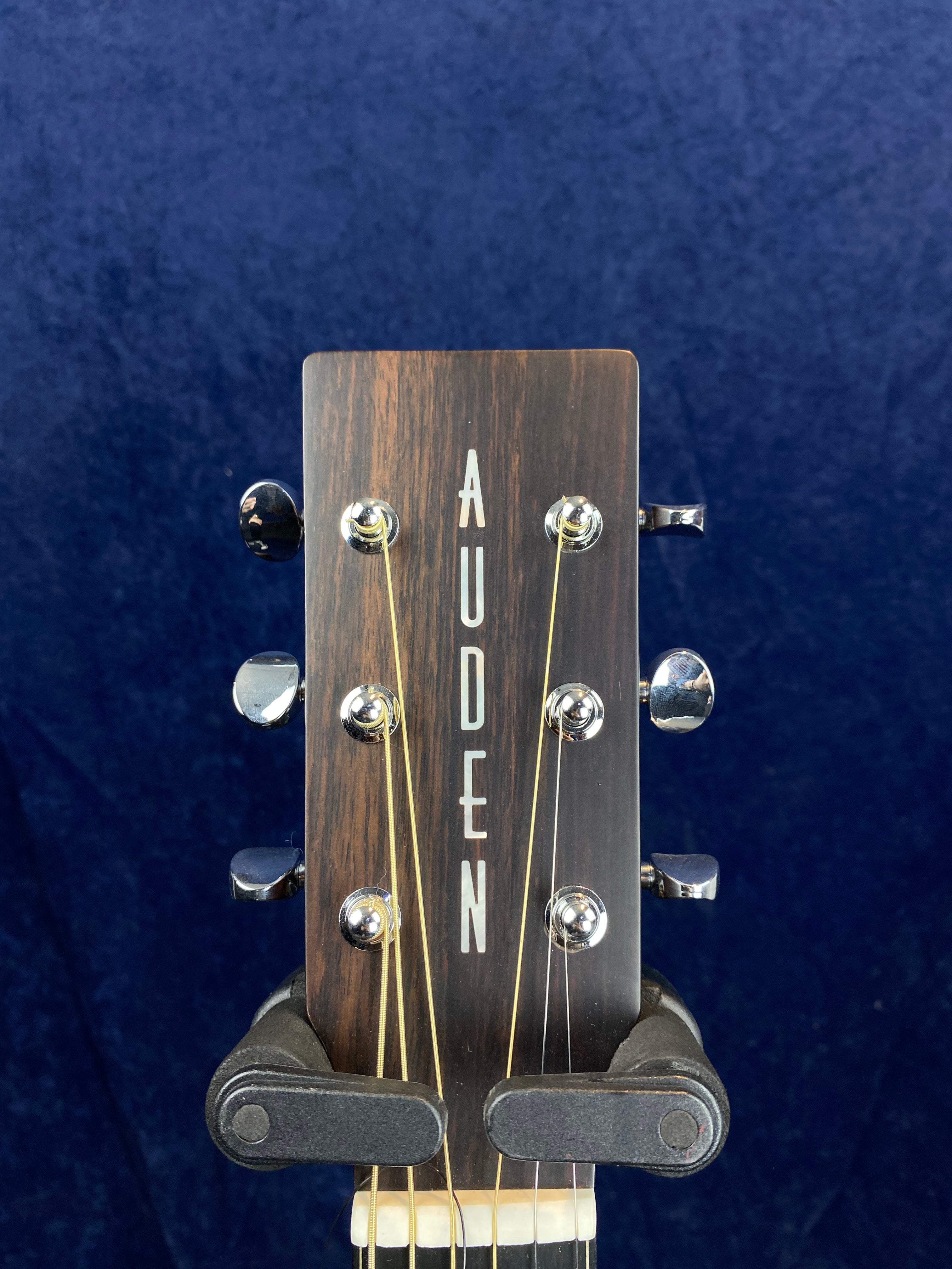 Close-up of an Auden acoustic guitar headstock with six tuning pegs, dark wood finish, and the brand name vertically inlaid in white letters.