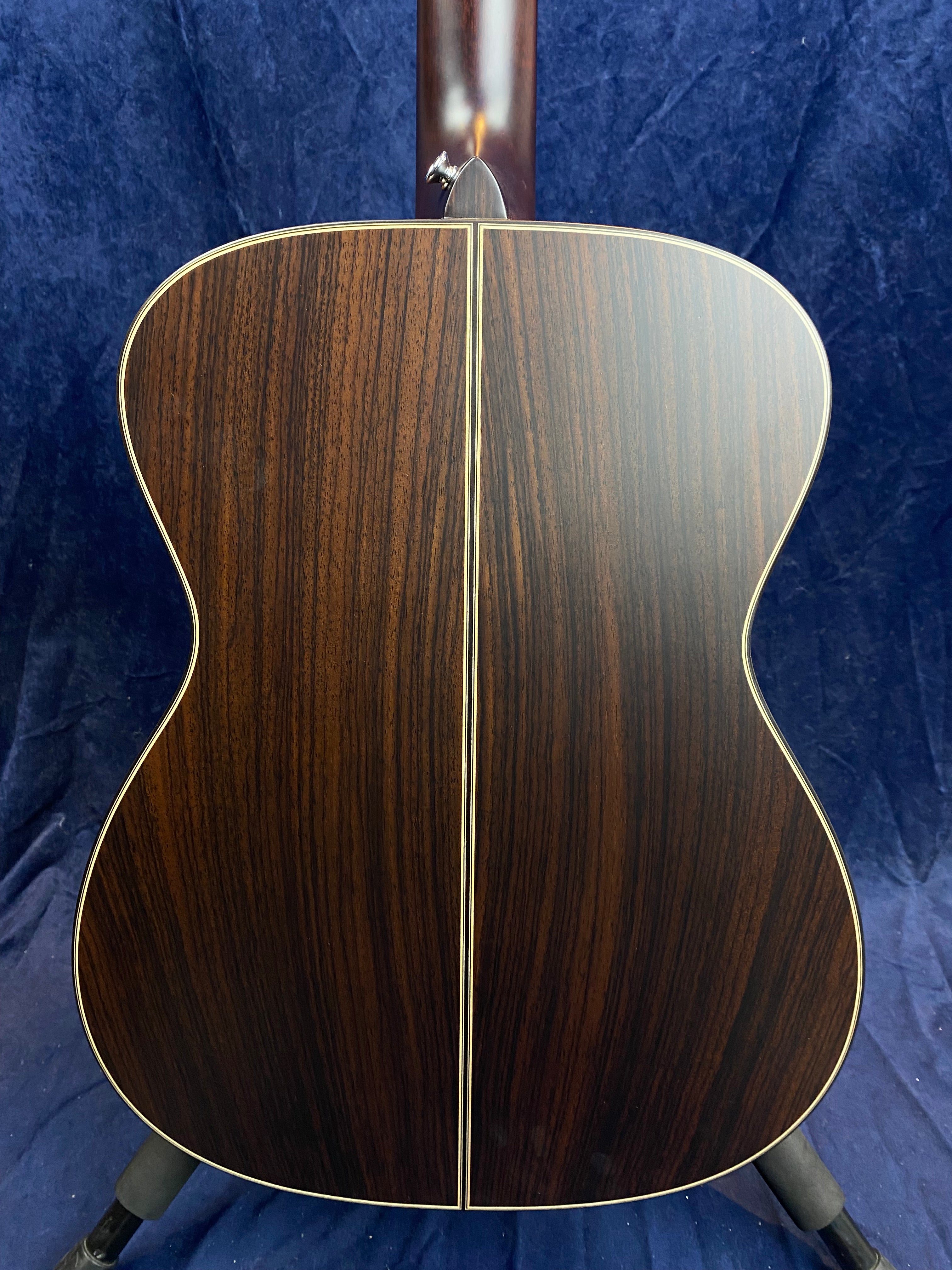 Acoustic guitar back view showing dark wood with a straight vertical divider and subtle grain patterns, bordered by thin pale binding.