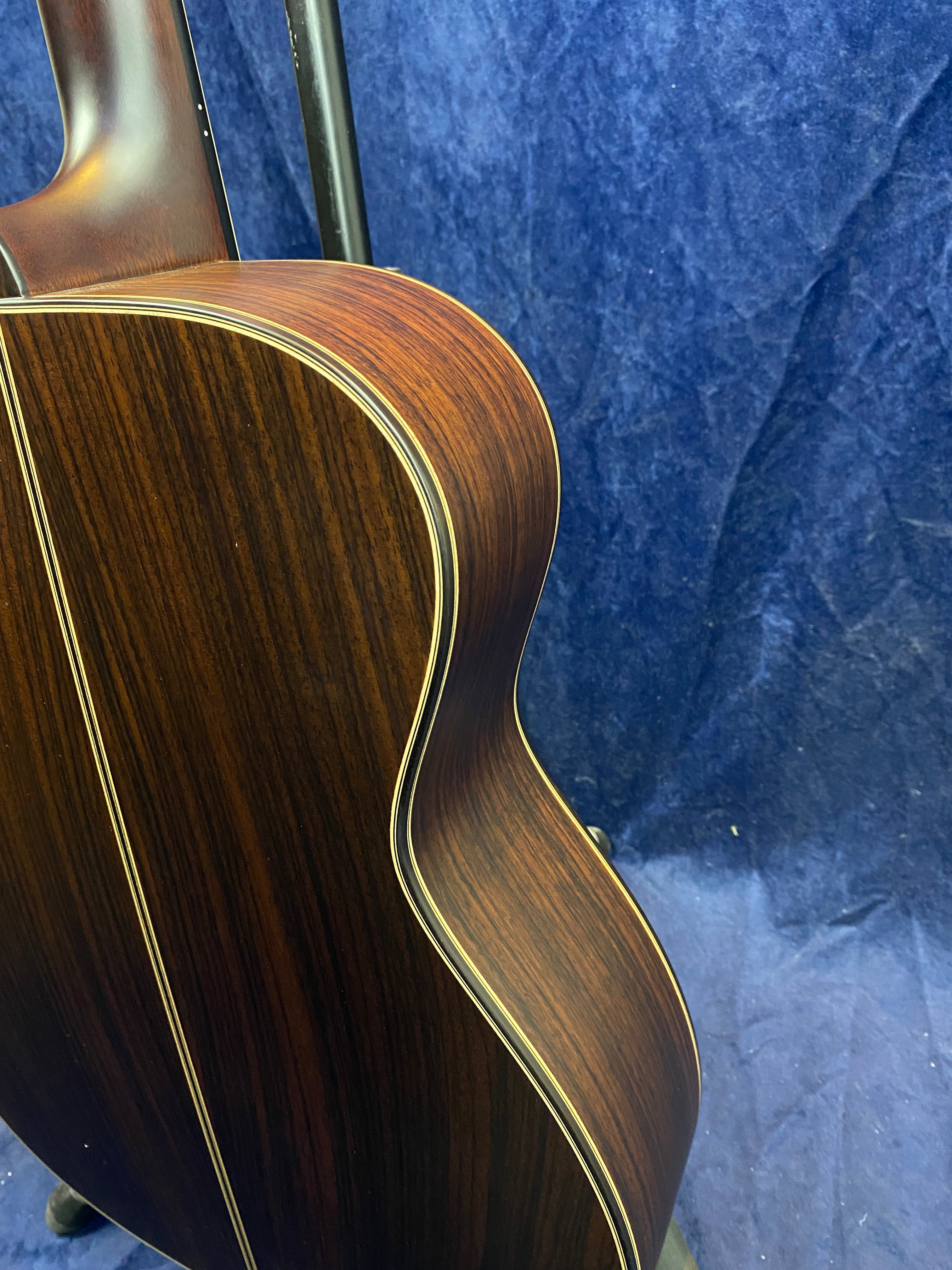 Curved side view of an acoustic guitar with dark, striped wood grain and light binding against a blue textured background.