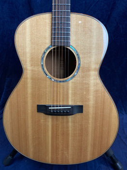 Light brown acoustic guitar with a glossy wood finish, a round sound hole bordered by abalone inlay, six strings, and a dark wooden bridge with white bridge pins.