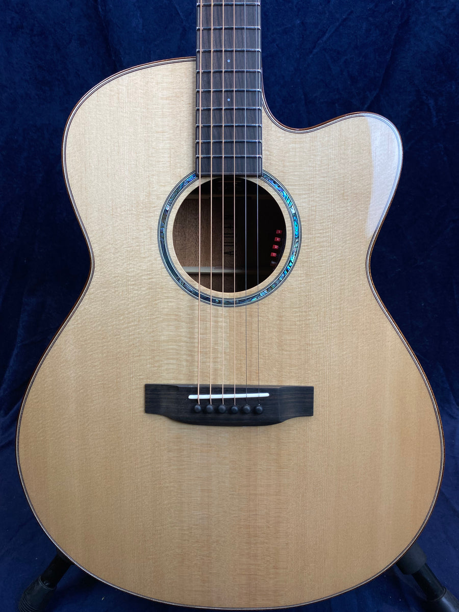 Light wood acoustic guitar with a cutaway body, six strings, black bridge, and decorative blue-green inlay around the soundhole.