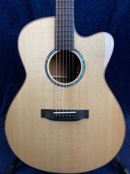 Light wood acoustic guitar with a cutaway body, six strings, black bridge, and decorative blue-green inlay around the soundhole.