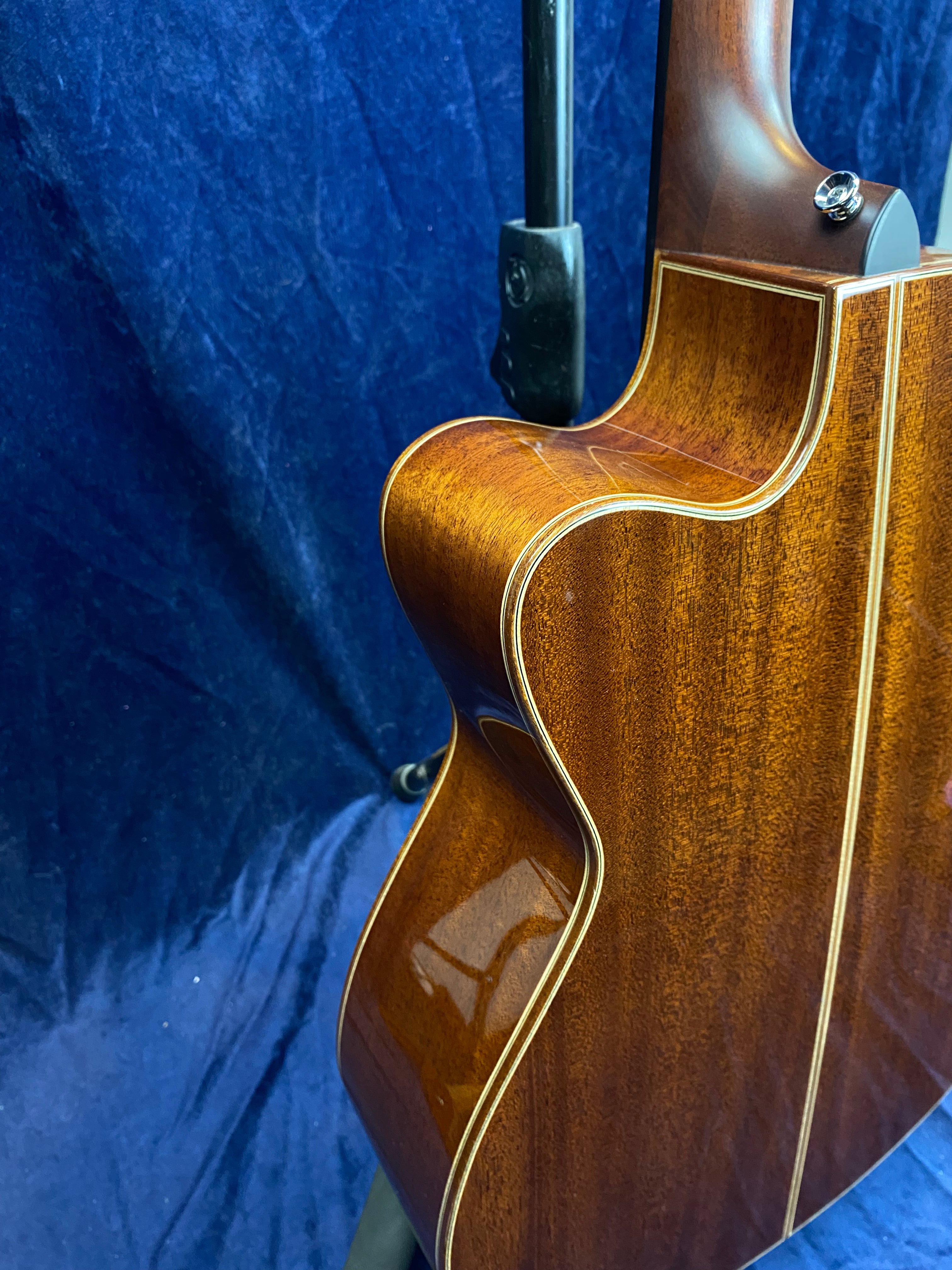 Glossy, rich brown acoustic guitar body with cream binding, cutaway design, and wood grain detail, shown against a dark blue background.