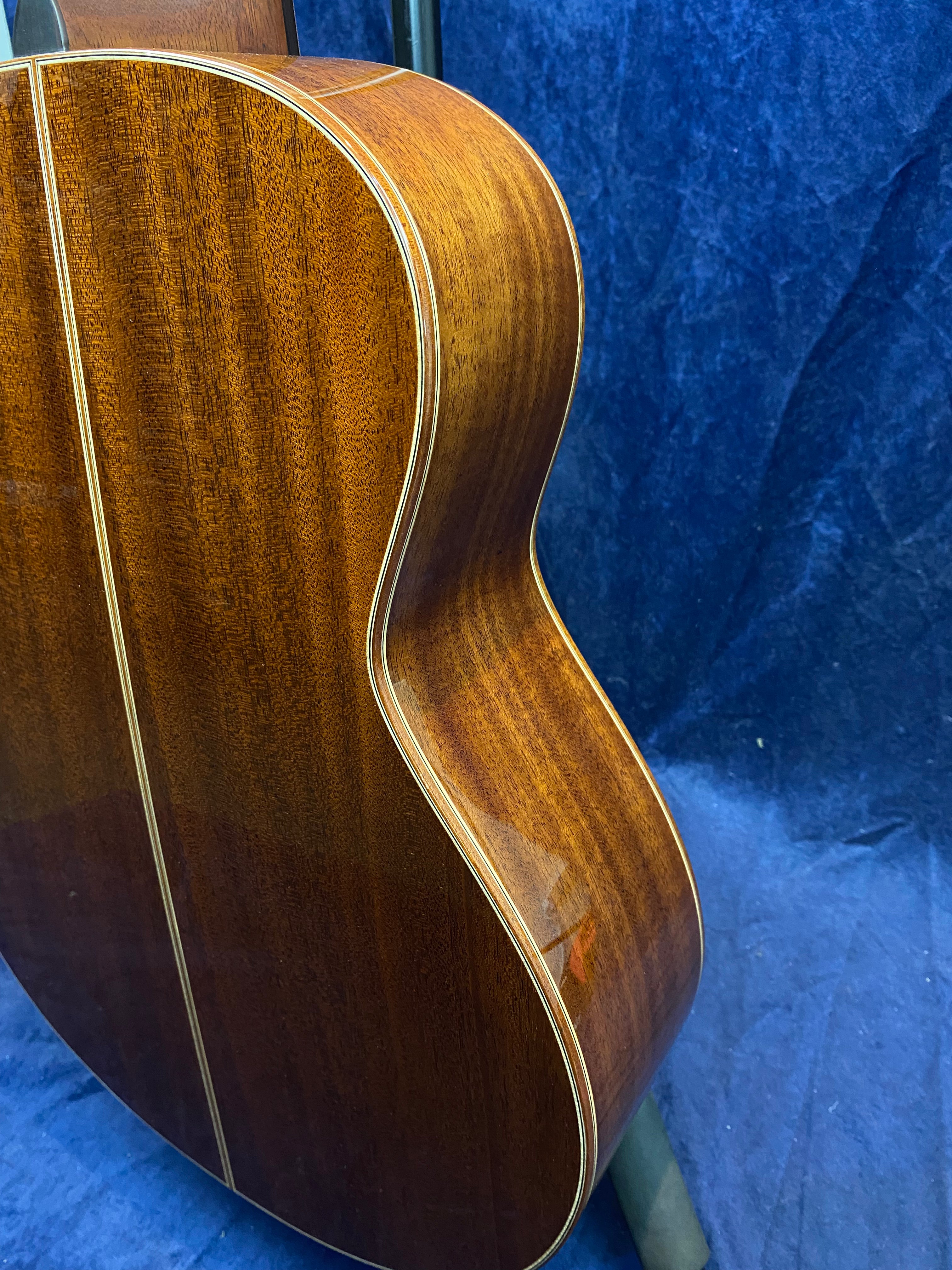 Curved, polished wooden back of an acoustic guitar with a light inlay strip running down the center against a dark blue background.