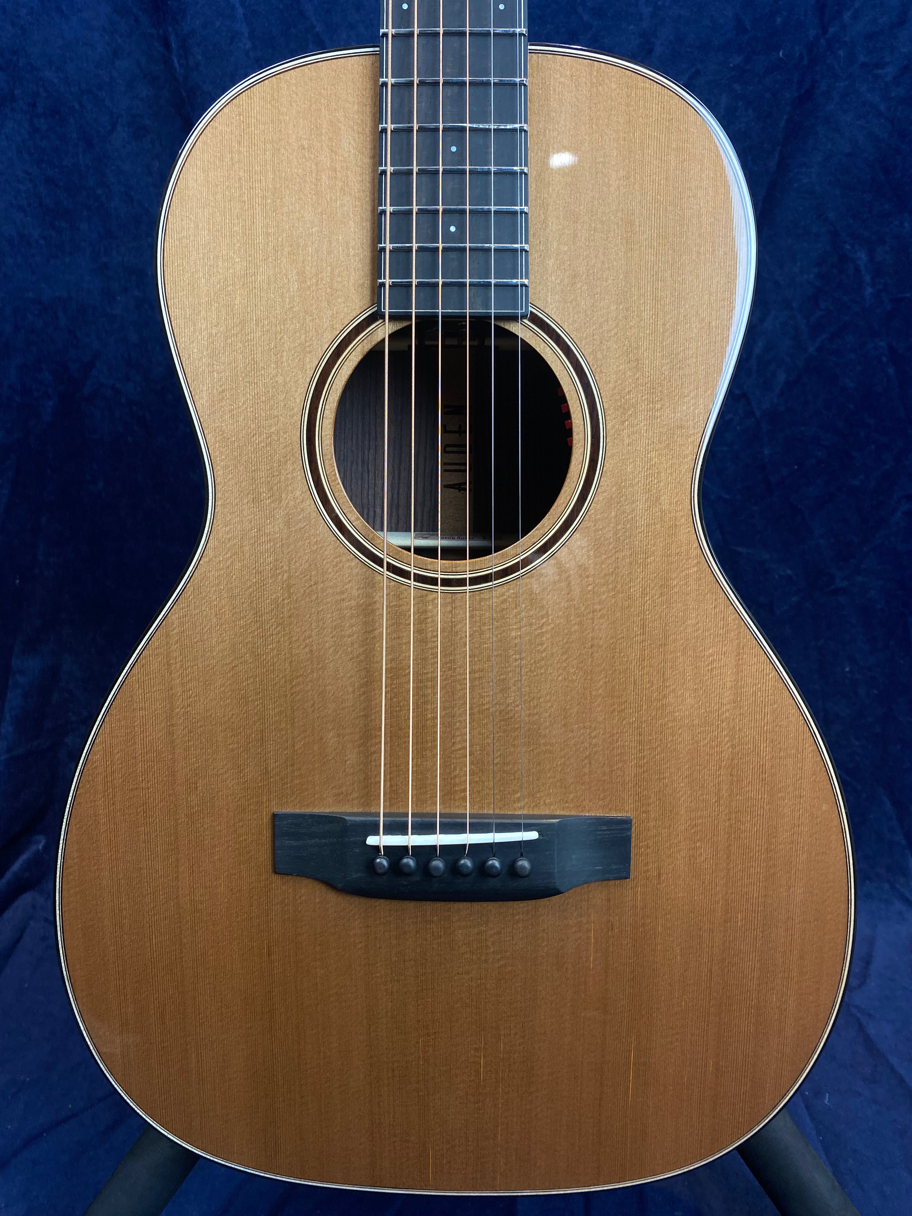 Acoustic guitar with a glossy natural wood finish, six strings, black bridge with white pins, and circular sound hole surrounded by a double-ring inlay.