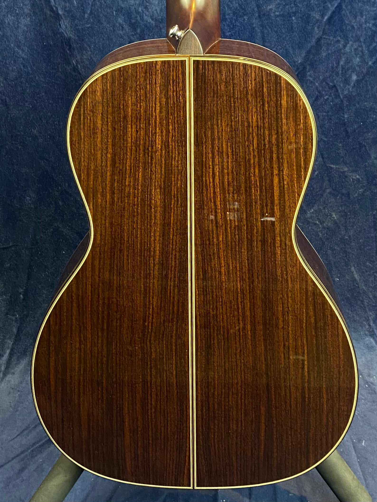 Back of an acoustic guitar made of dark wood with a straight vertical center seam, contrasted by pale wood binding along the edges.