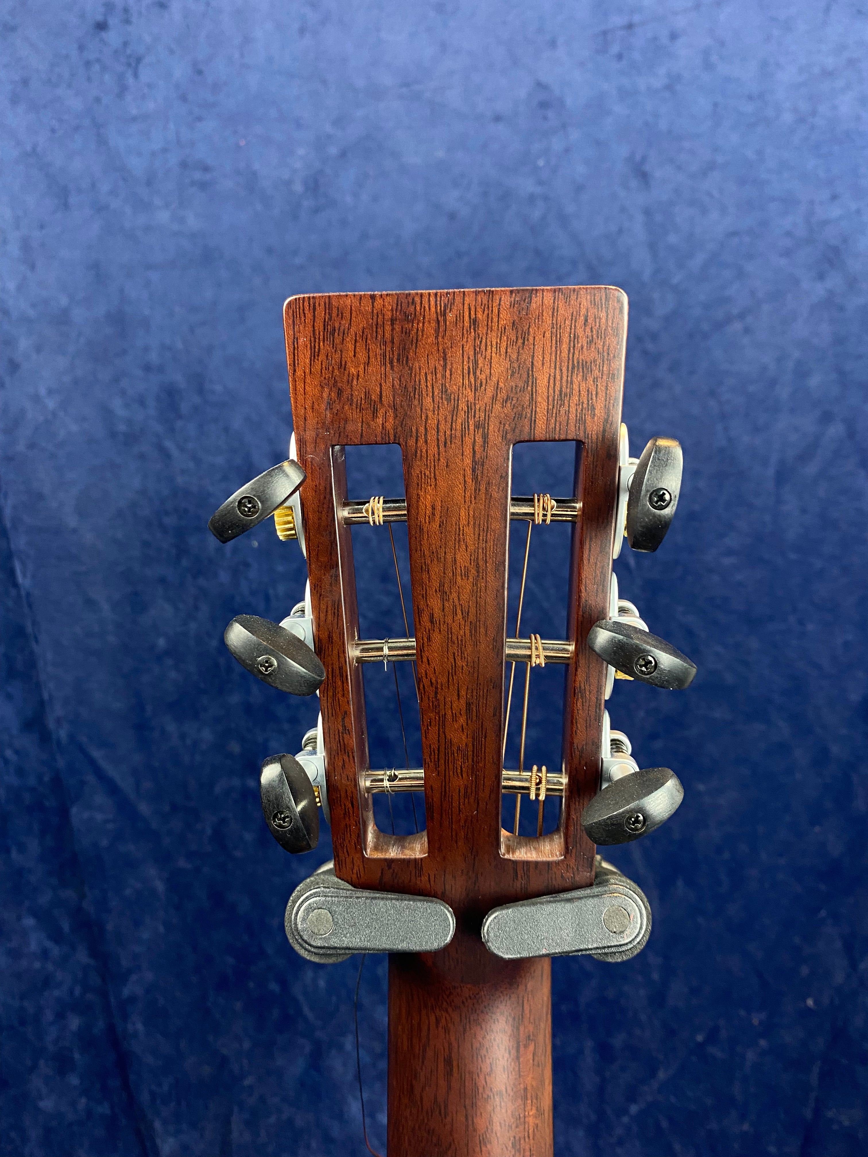 Six black tuning pegs on the slotted wooden headstock of an acoustic guitar, shown against a dark blue textured background.