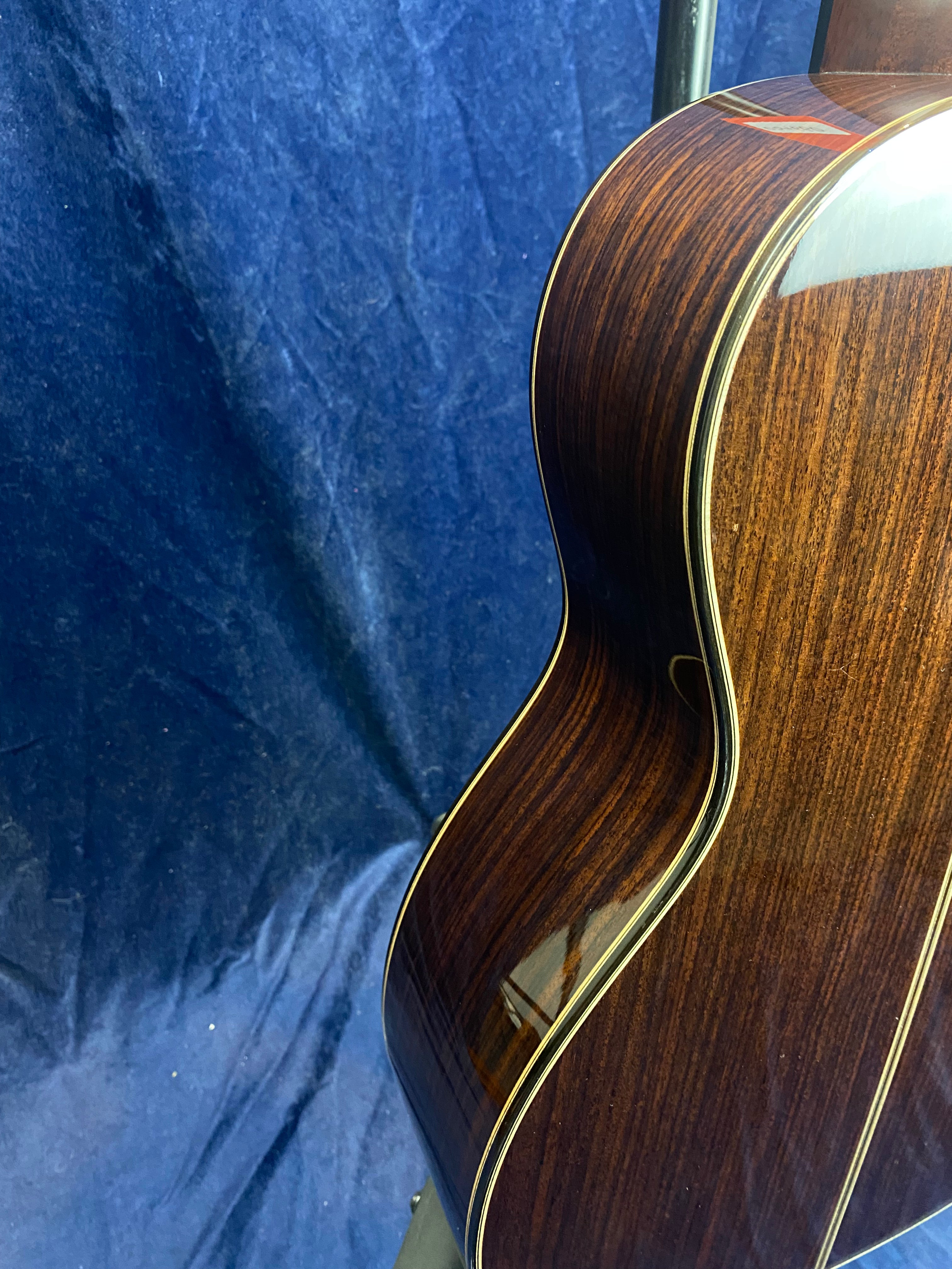 Glossy acoustic guitar body with dark wood grain and cream binding, shown against a blue textured background.