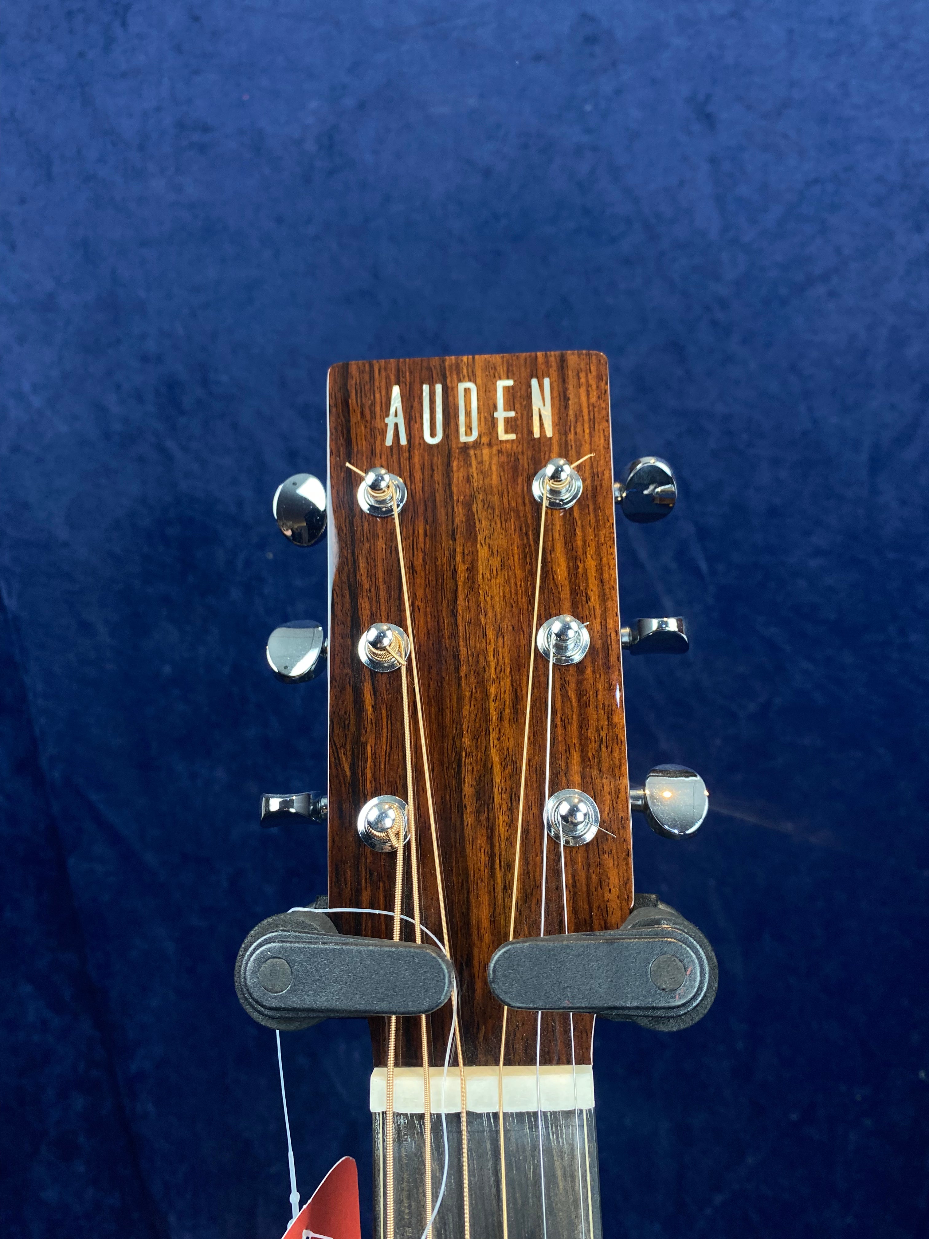 Close-up of an Auden acoustic guitar headstock with six tuning pegs against a dark blue background.