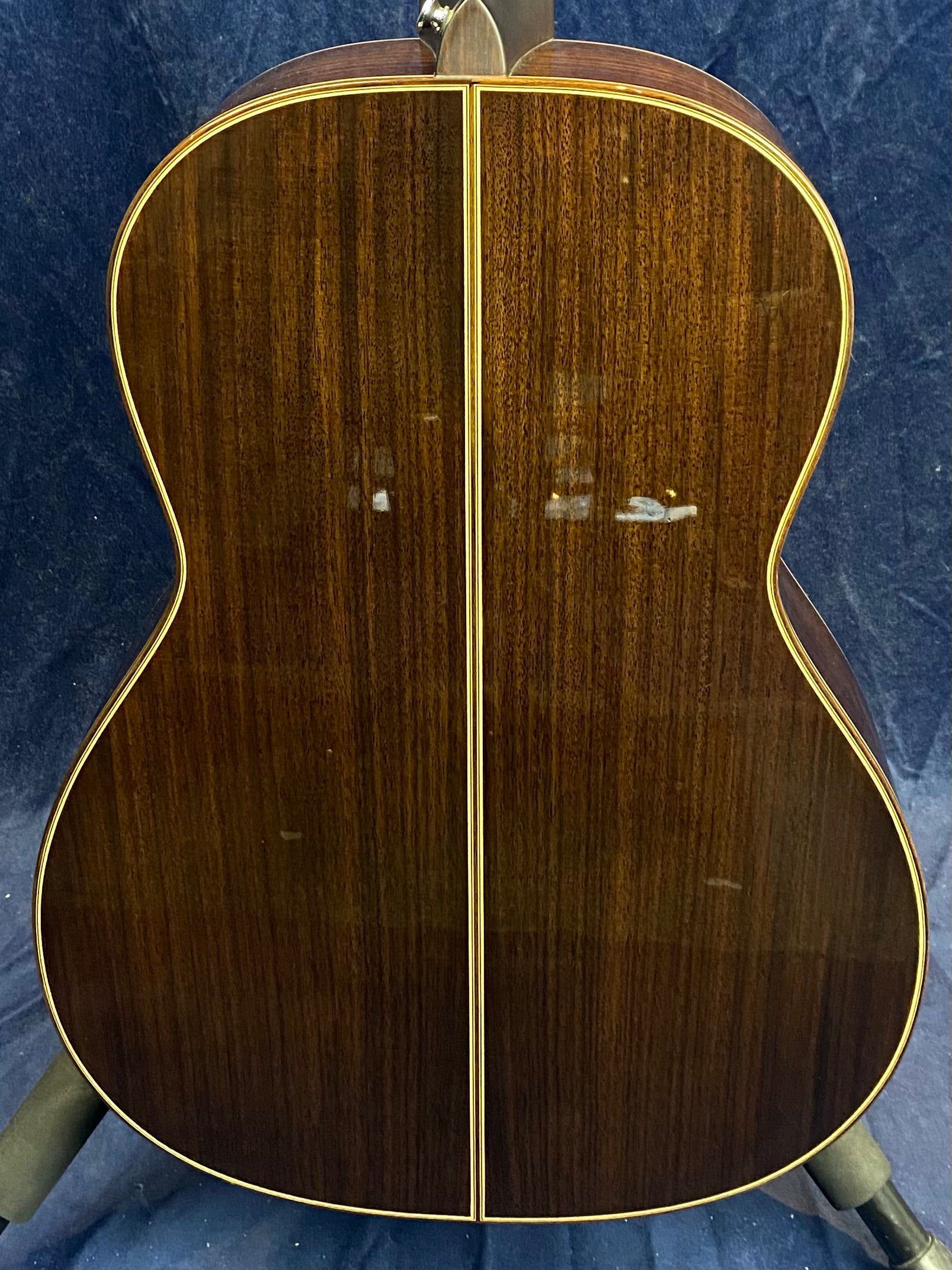 Back of an acoustic guitar with glossy dark wood, a vertical center seam, and light-colored binding outlining the body.