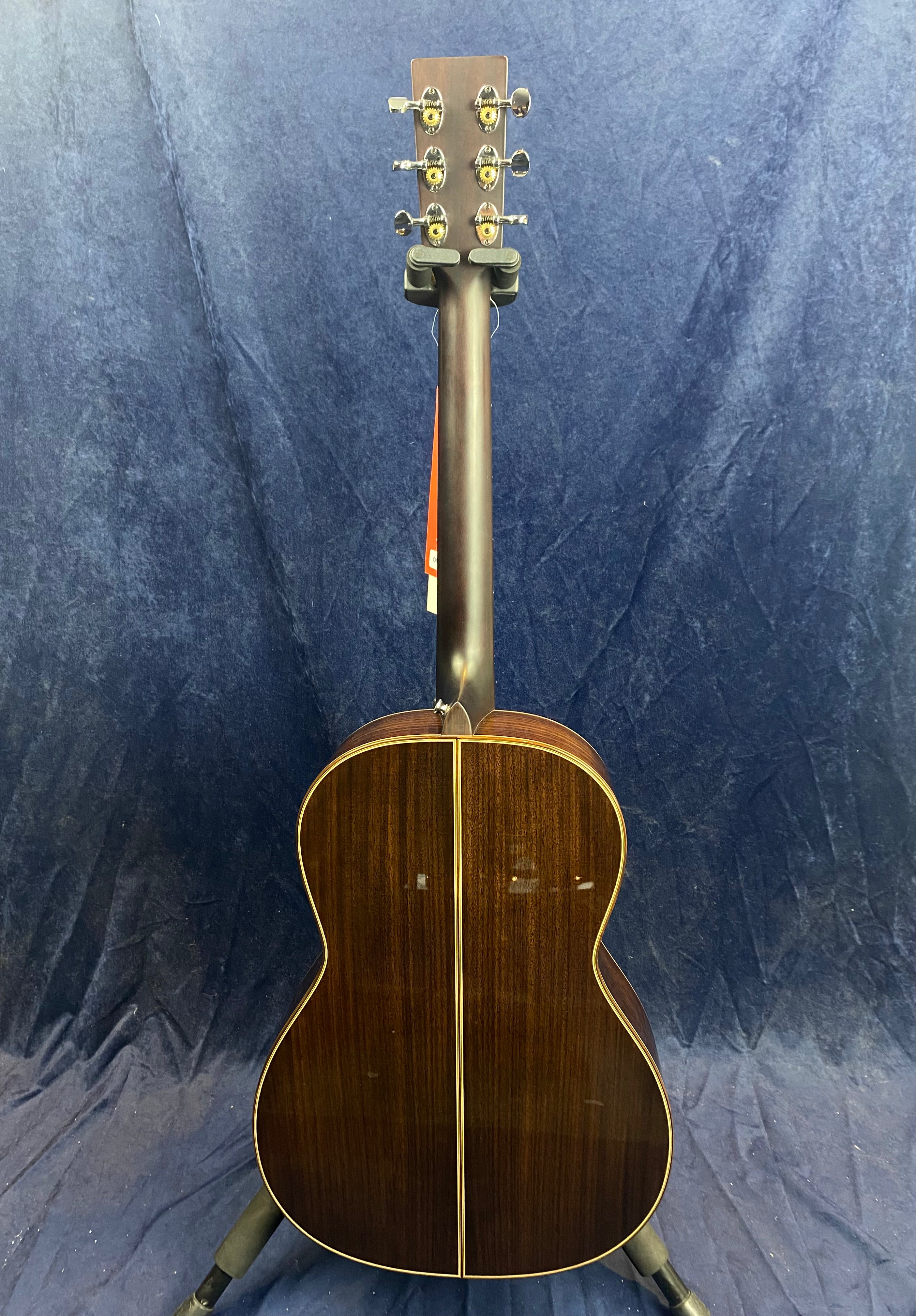 Dark wood acoustic guitar seen from the back, with a glossy finish and a thin light stripe running down the center of the body.