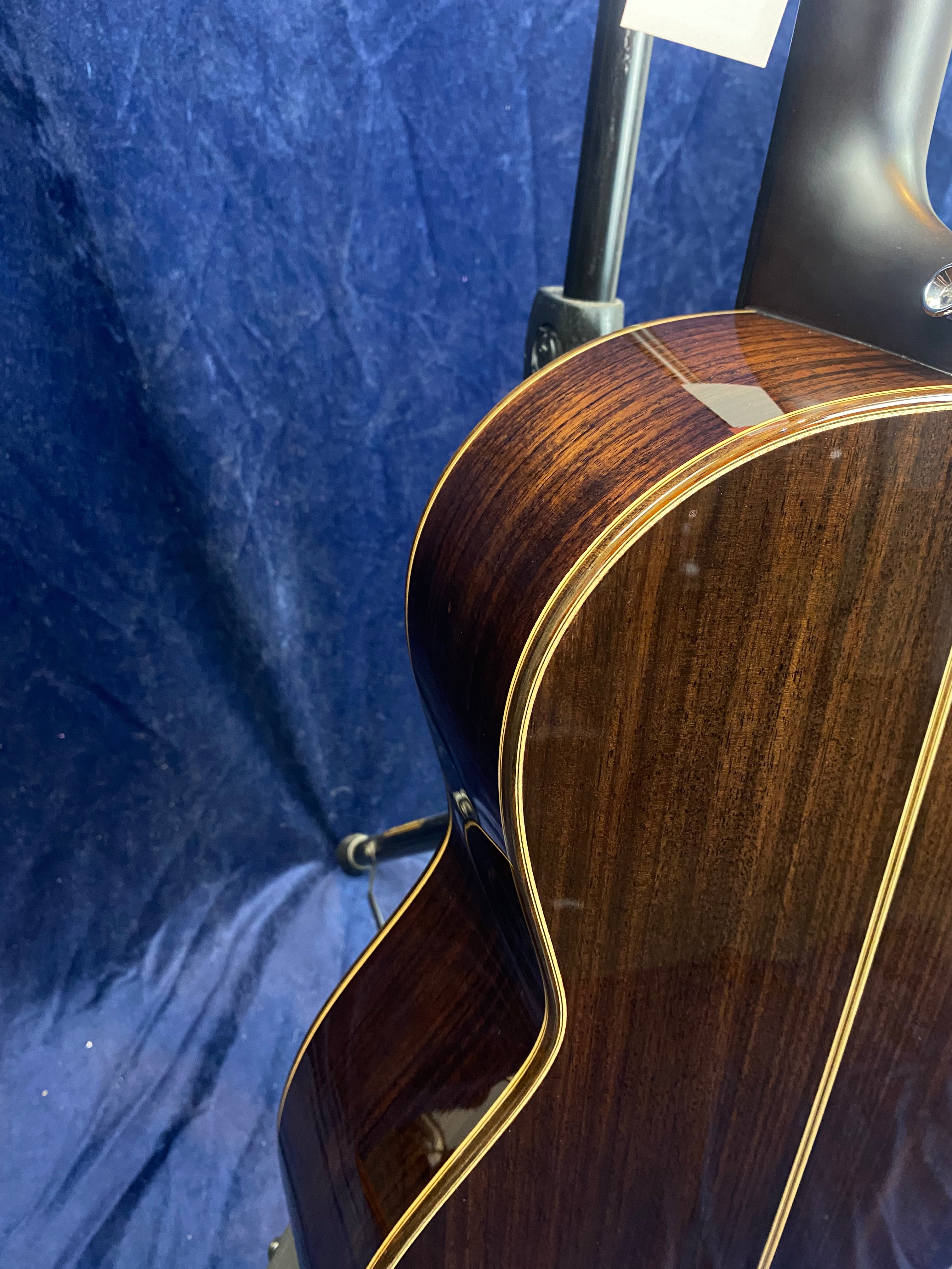 Dark wood acoustic guitar body with a glossy finish and cream-colored binding, shown from the side against a dark blue background.