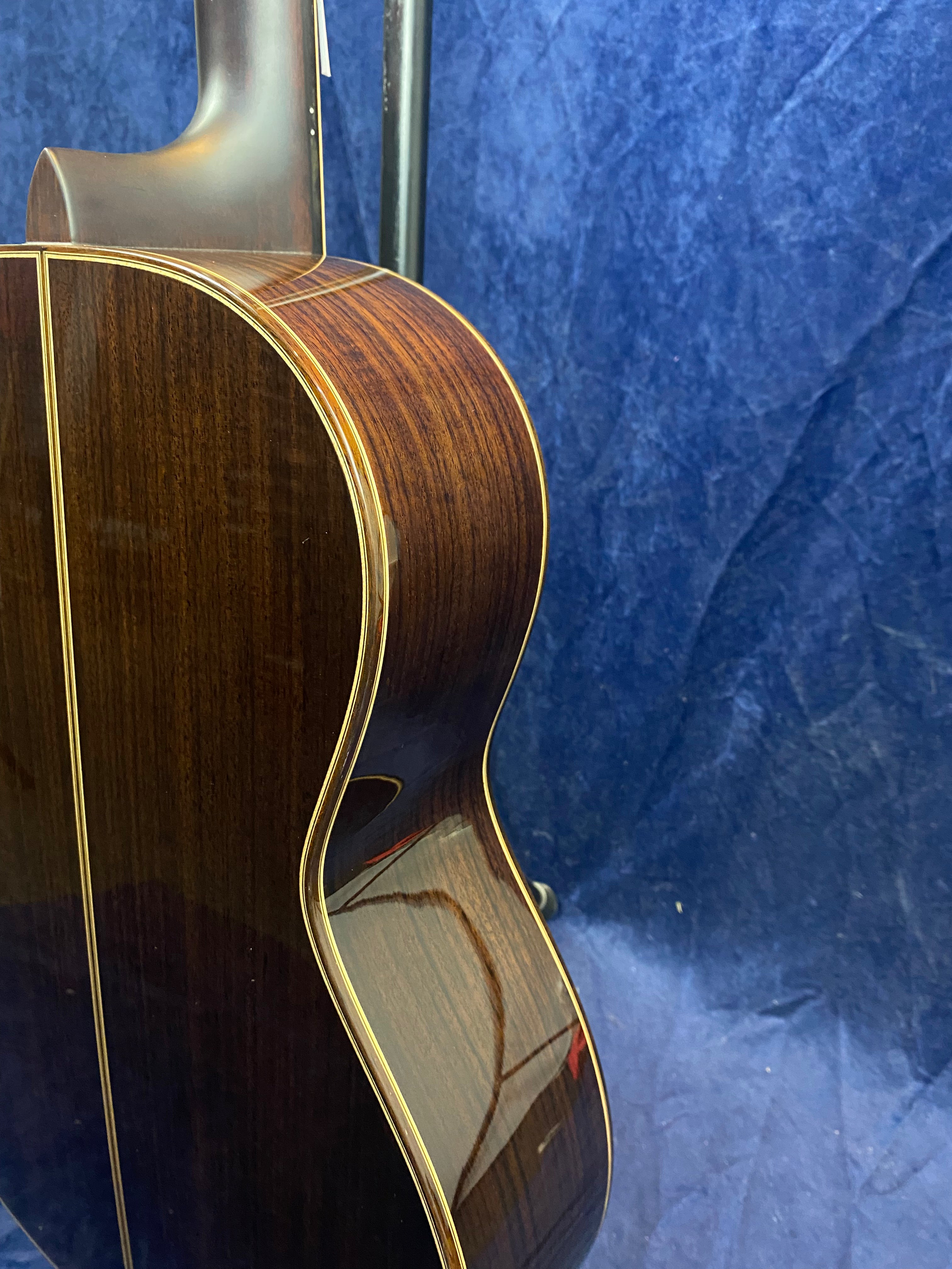 Glossy dark wood acoustic guitar body with light binding, shown from the side and back against a blue textured background.