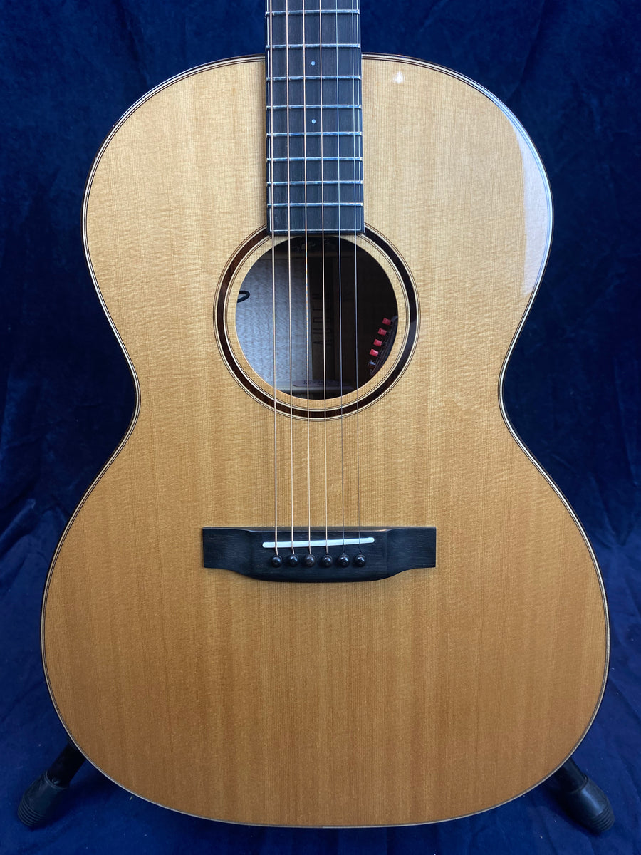 Natural wood acoustic guitar with six strings, a round sound hole, and a dark bridge, shown against a dark blue background.