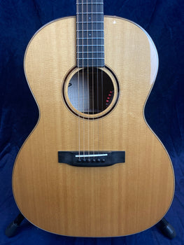 Natural wood acoustic guitar with six strings, a round sound hole, and a dark bridge, shown against a dark blue background.