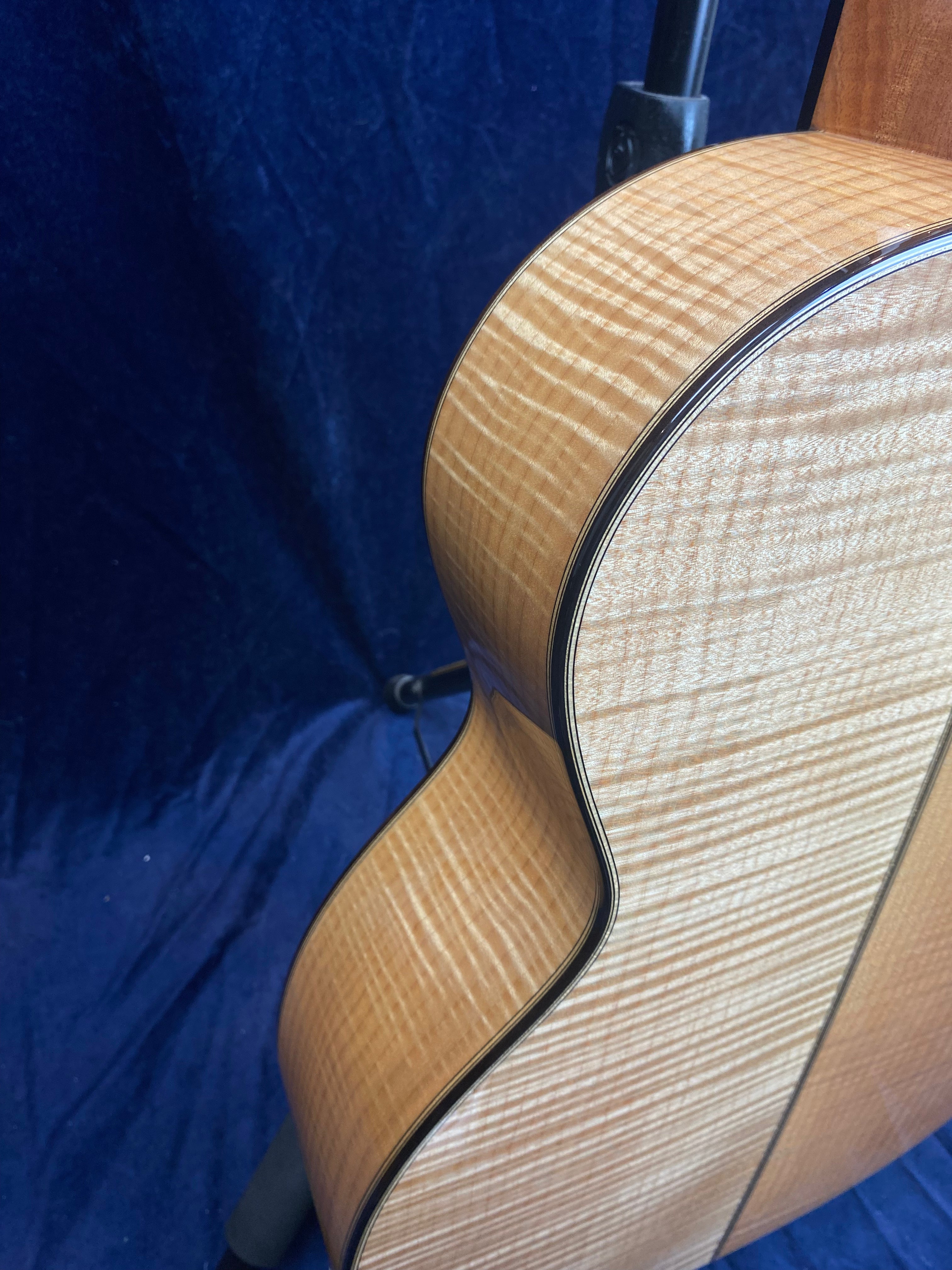Curved side and back of an acoustic guitar showing glossy, light-colored wood with pronounced wavy grain patterns and dark edge binding.
