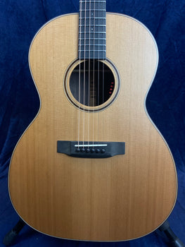 Light wood acoustic guitar with a round sound hole, black bridge, and white-edged body, strings stretching from bridge to fretboard.