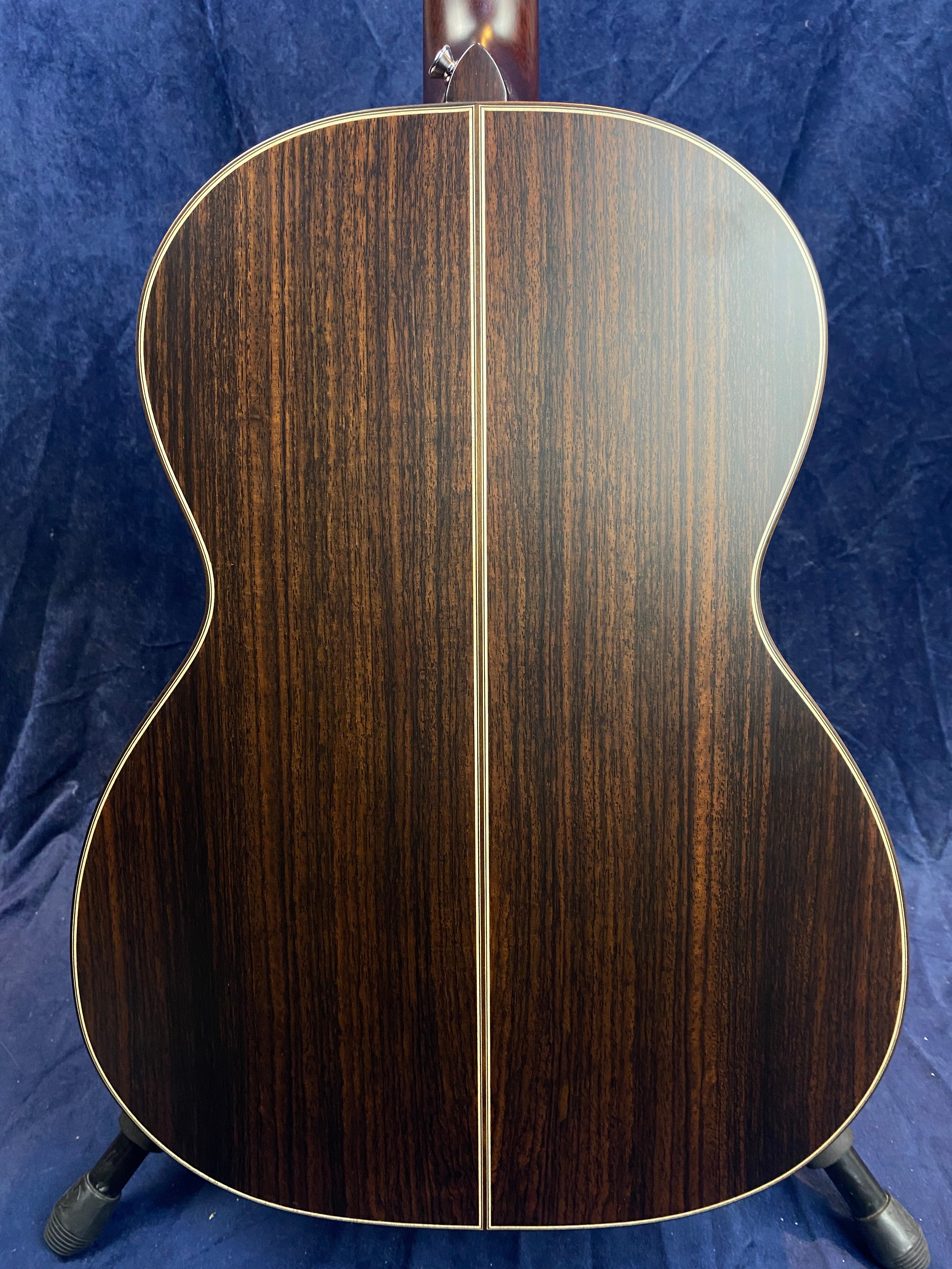 The back of an acoustic guitar with dark brown wood, fine vertical grain, and a thin light stripe running down the center.