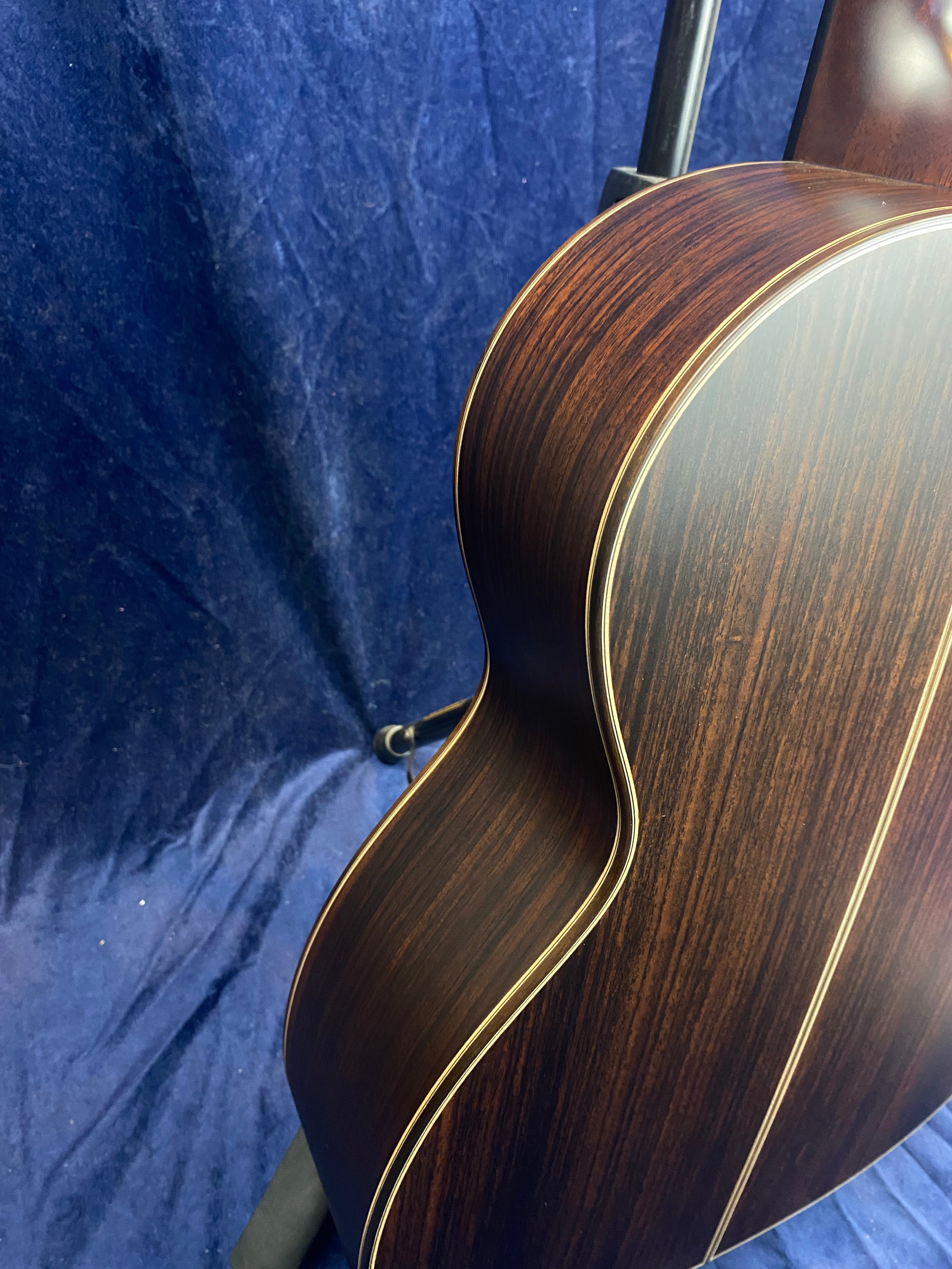 Dark wood acoustic guitar body with light wood inlay, set against a dark blue textured backdrop. Only the guitar side and back are visible.