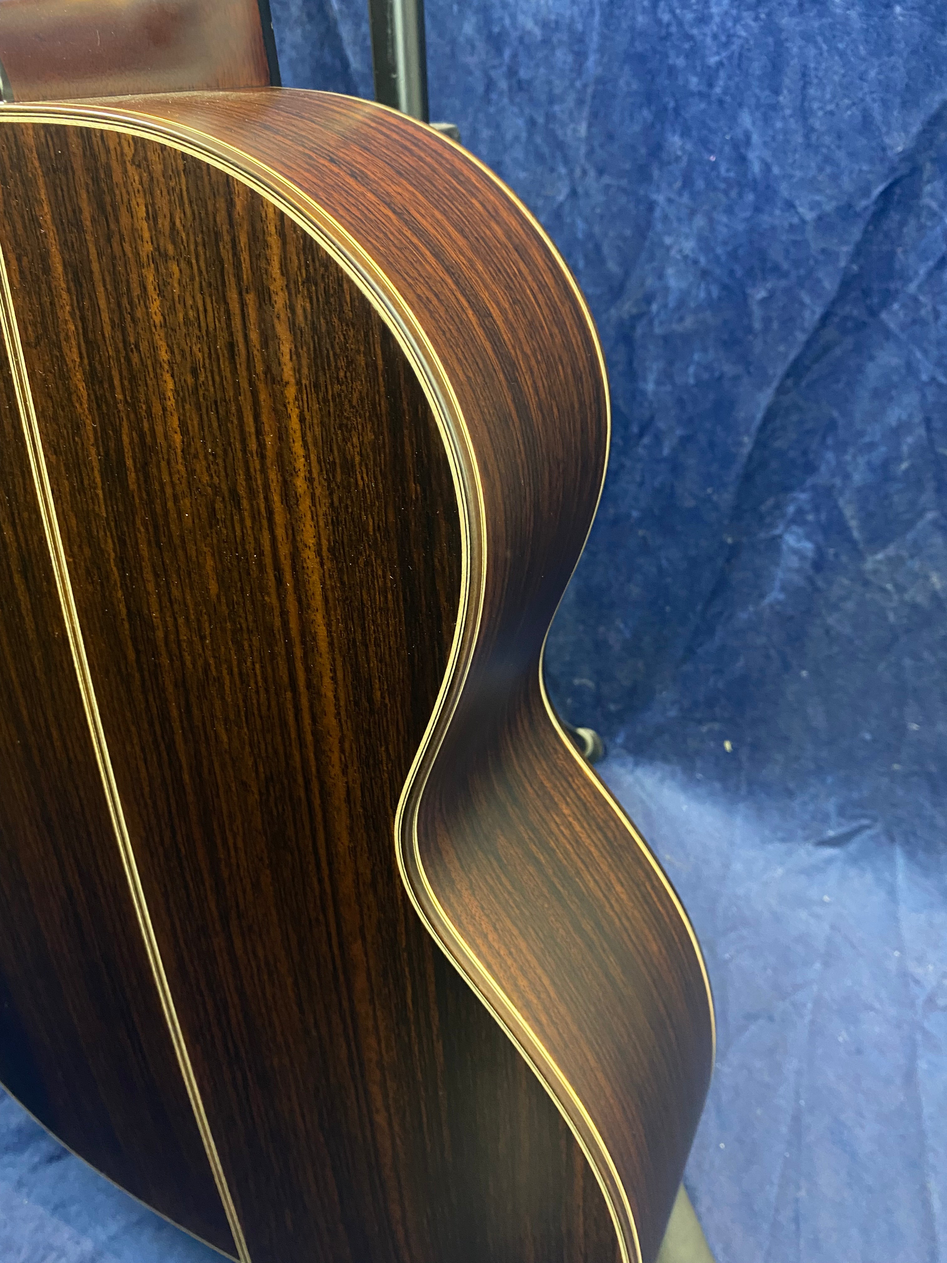 Dark brown acoustic guitar body with visible wood grain, cream binding along the edges, and a pronounced curve where the guitar narrows at the waist.