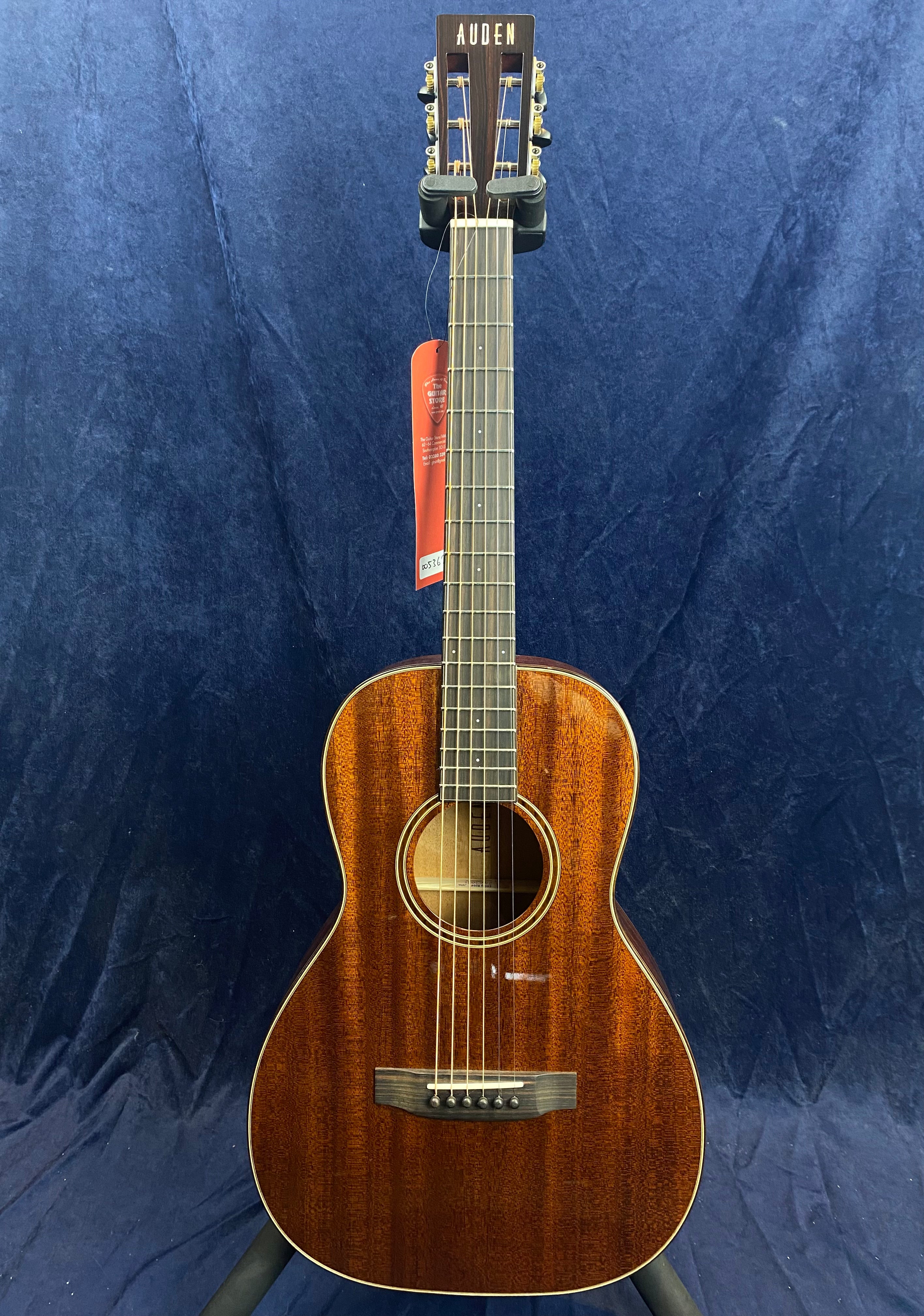 Small-bodied acoustic guitar with a glossy dark wood finish, six strings, round sound hole, and “AUDEN” inlaid on the headstock.