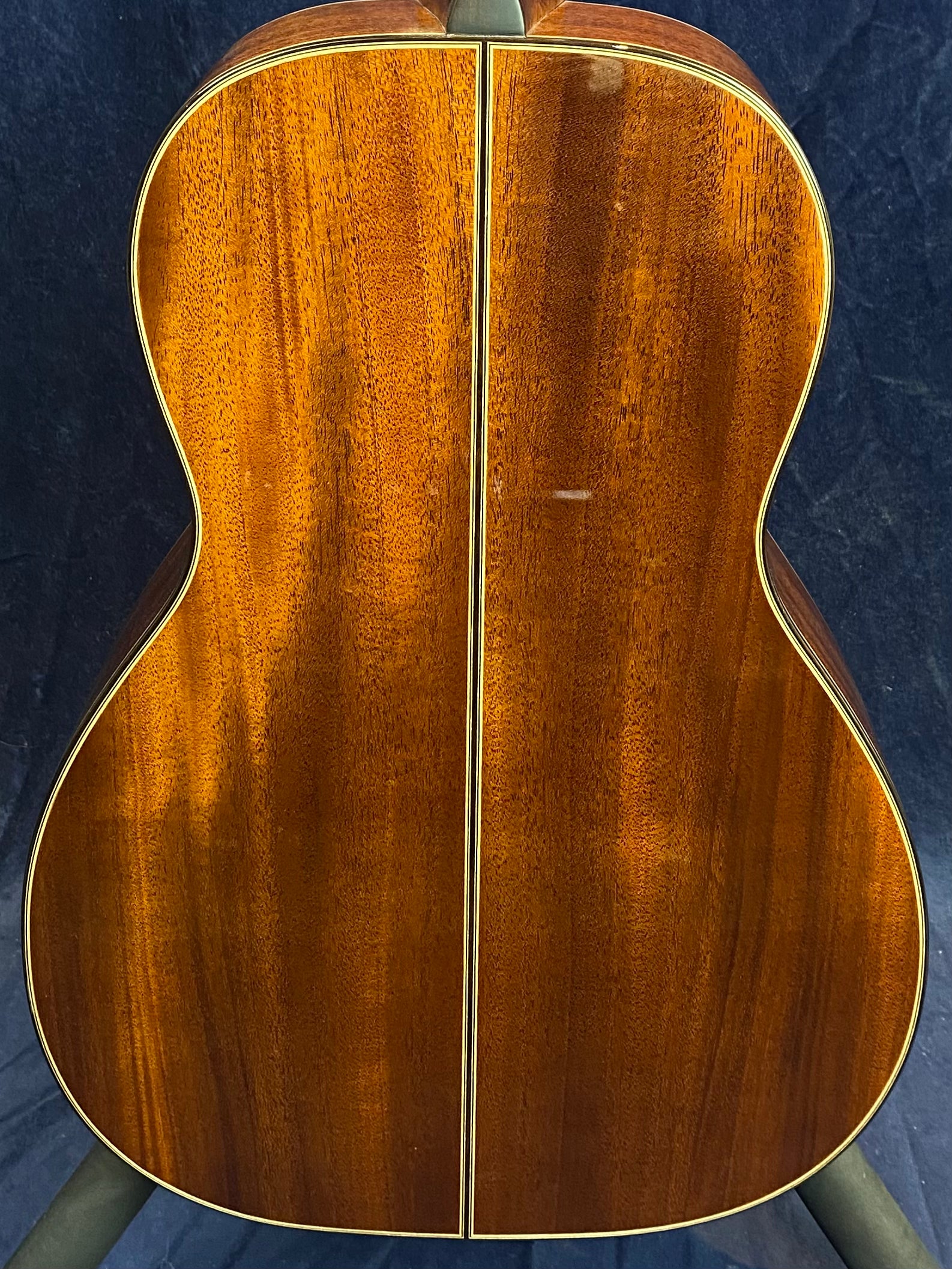 Glossy brown acoustic guitar back with a prominent center seam, golden wood grain, and cream-colored binding around the edges.