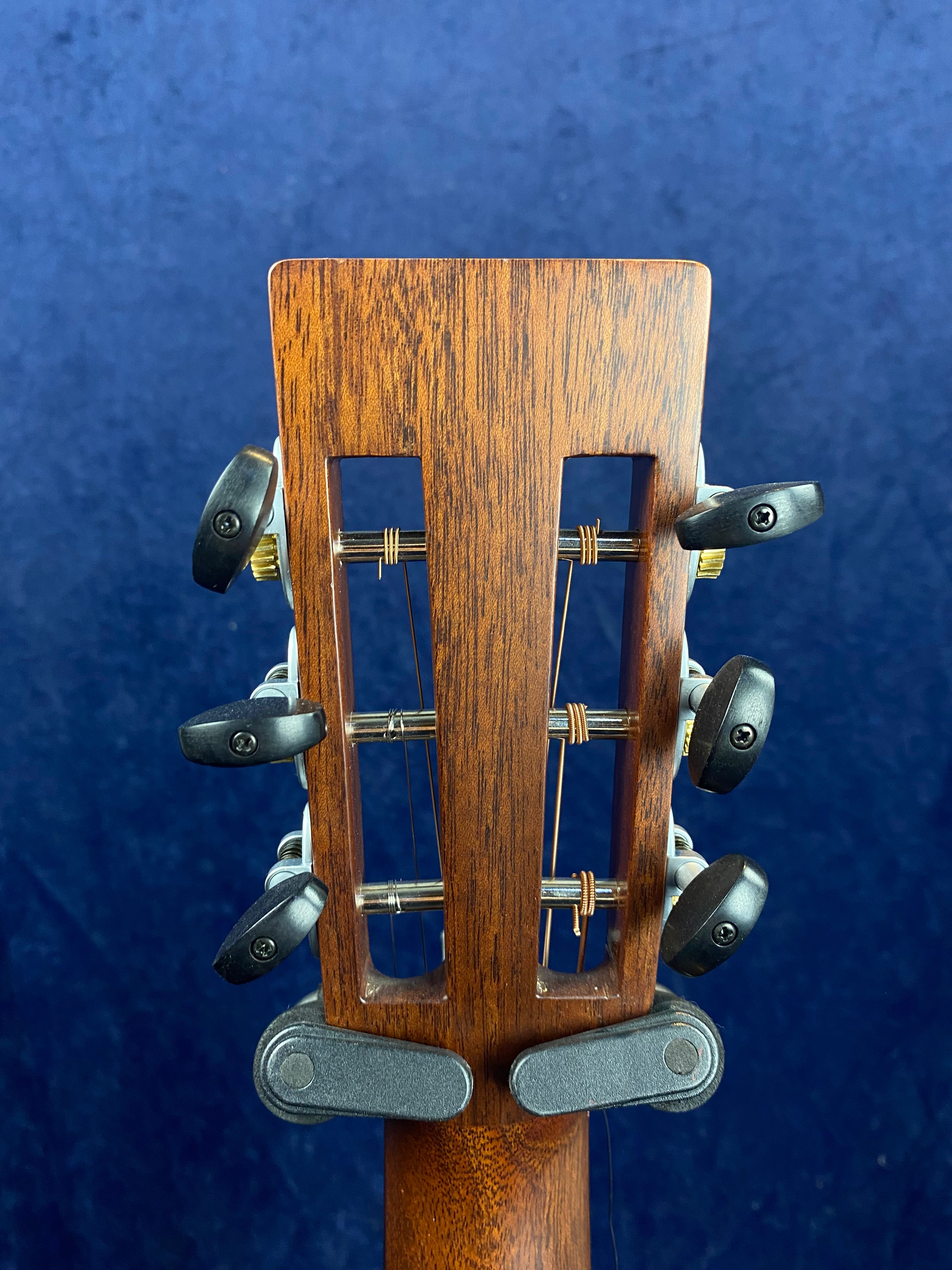 Slotted wooden acoustic guitar headstock with three black tuning pegs on each side, set against a blue background.