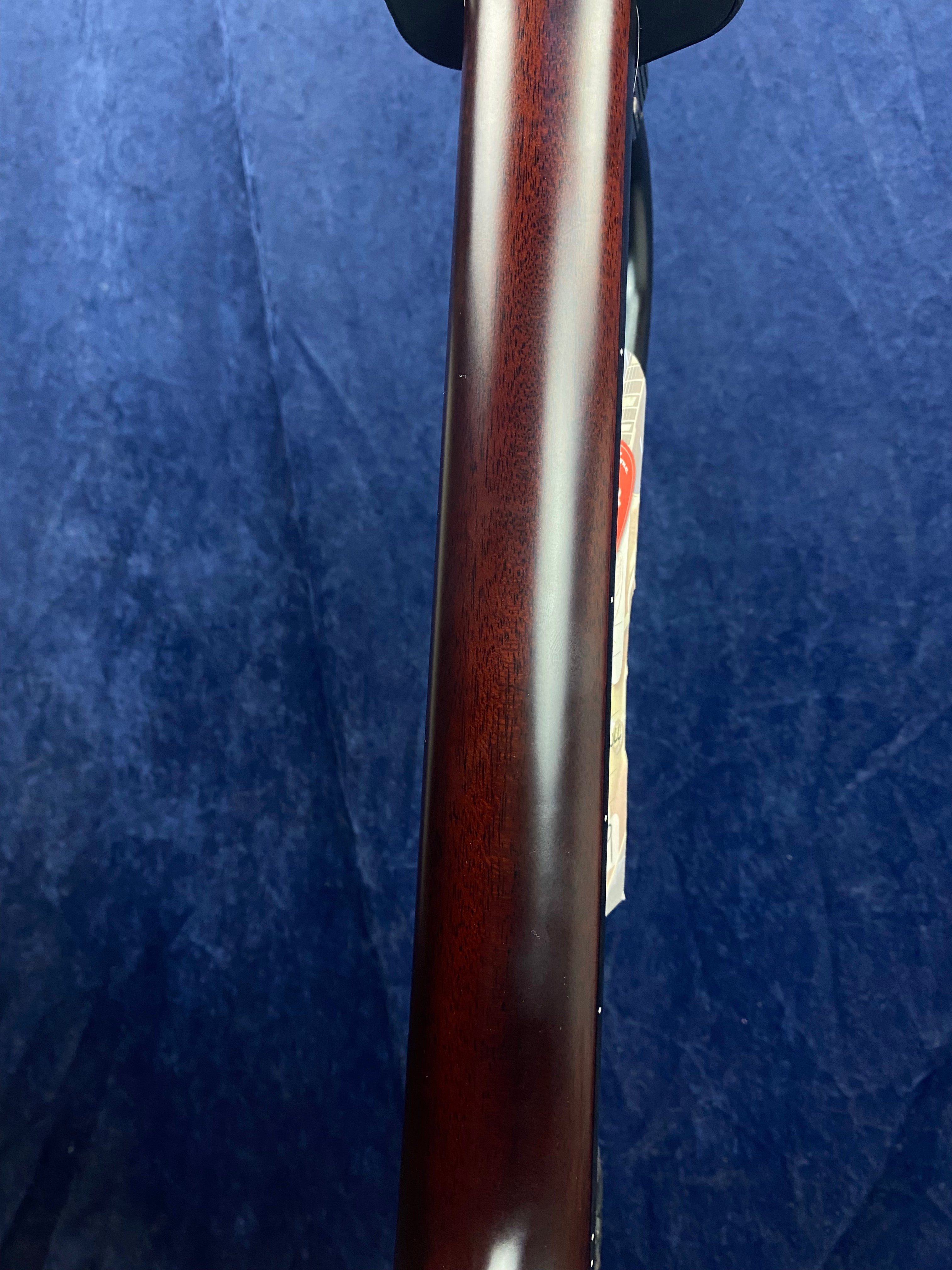 Smooth, polished dark brown acoustic guitar neck against a plain blue background, with a small paper tag partially visible on the side.