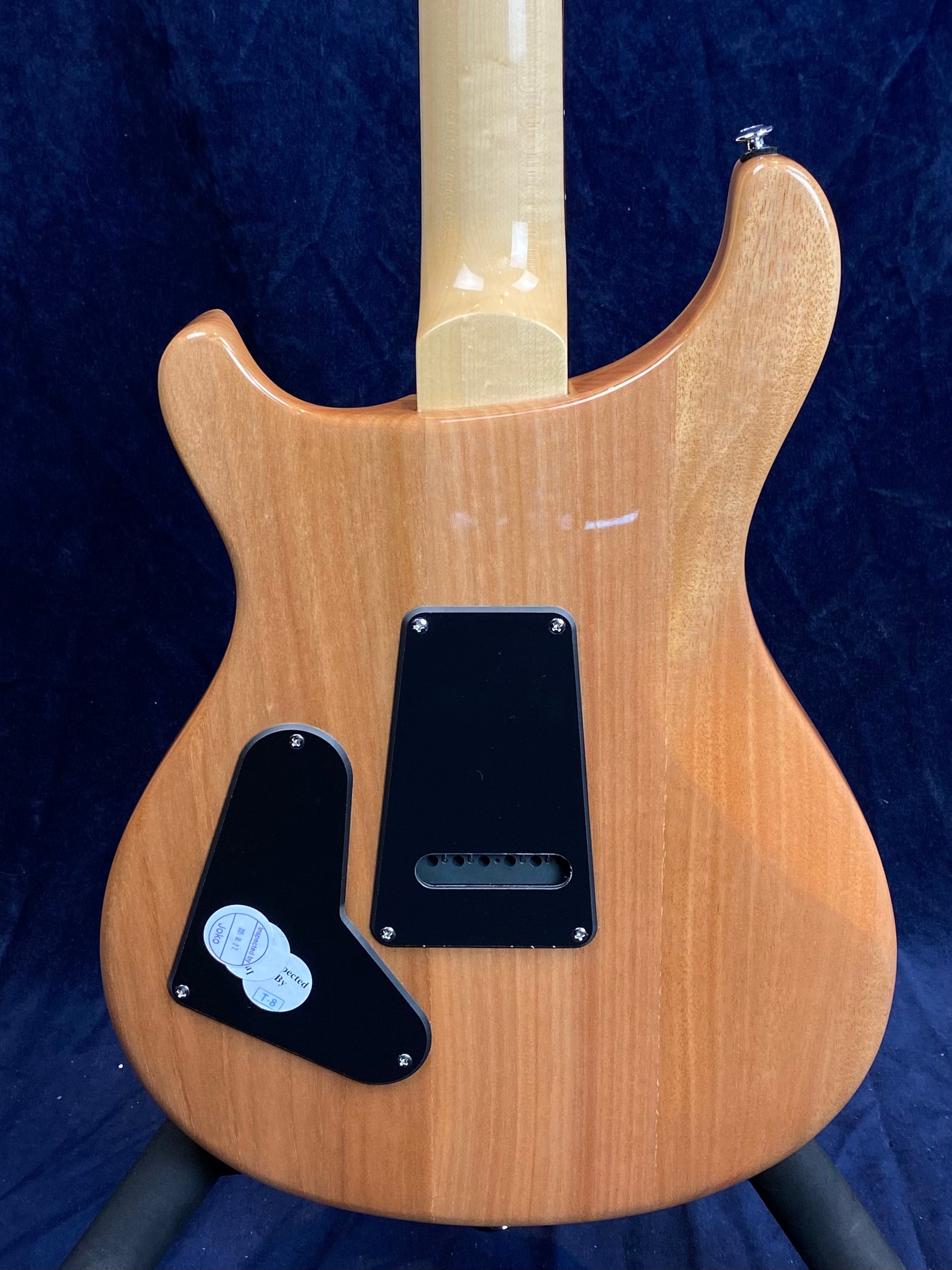 Natural wood finish electric guitar back, two black plastic covers for electronics and tremolo cavity, glossy light maple neck.