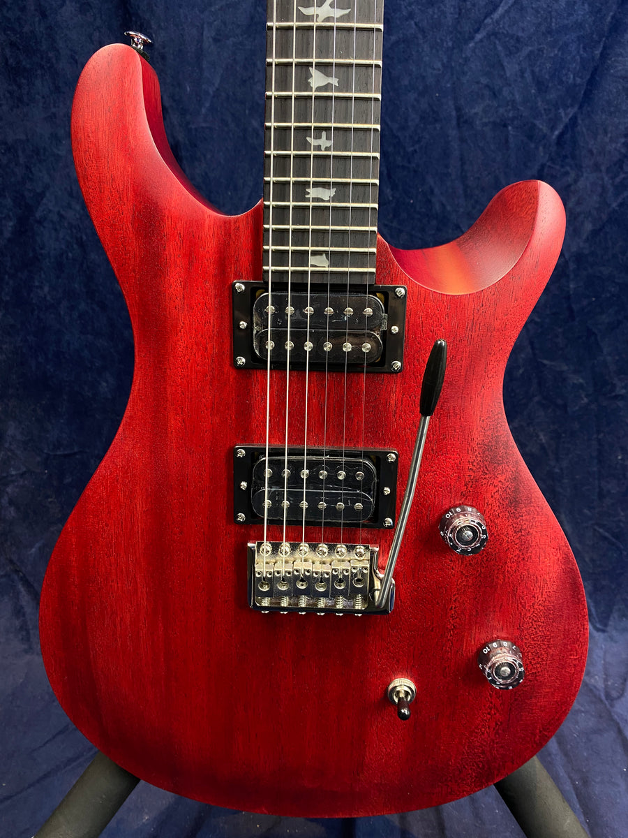 Red electric guitar with two black humbucker pickups, whammy bar, three control knobs, and bird inlays on the fretboard.