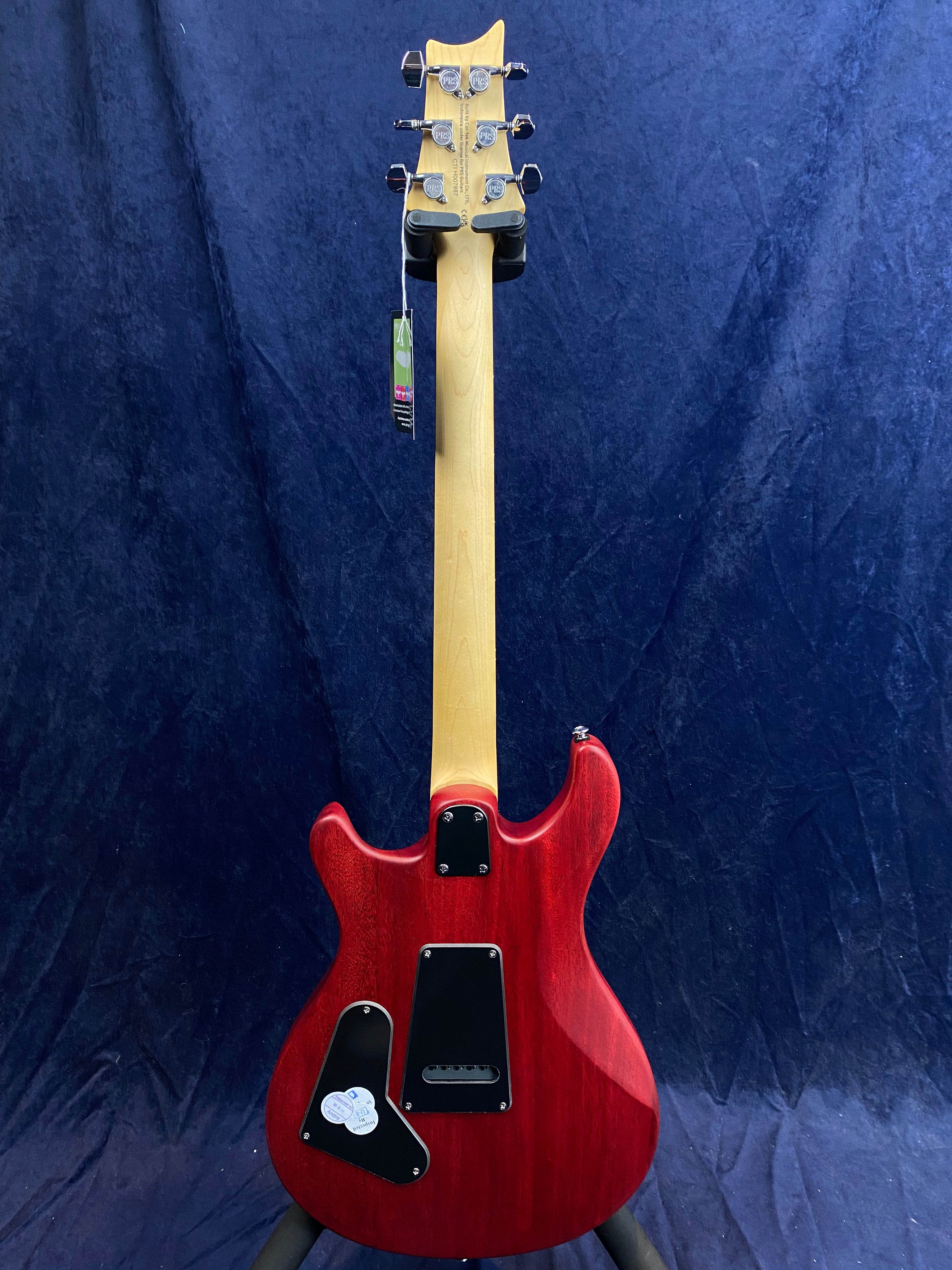 Electric guitar shown from the back with a red body, natural wood neck, chrome tuning pegs, and two black plastic covers on the body.