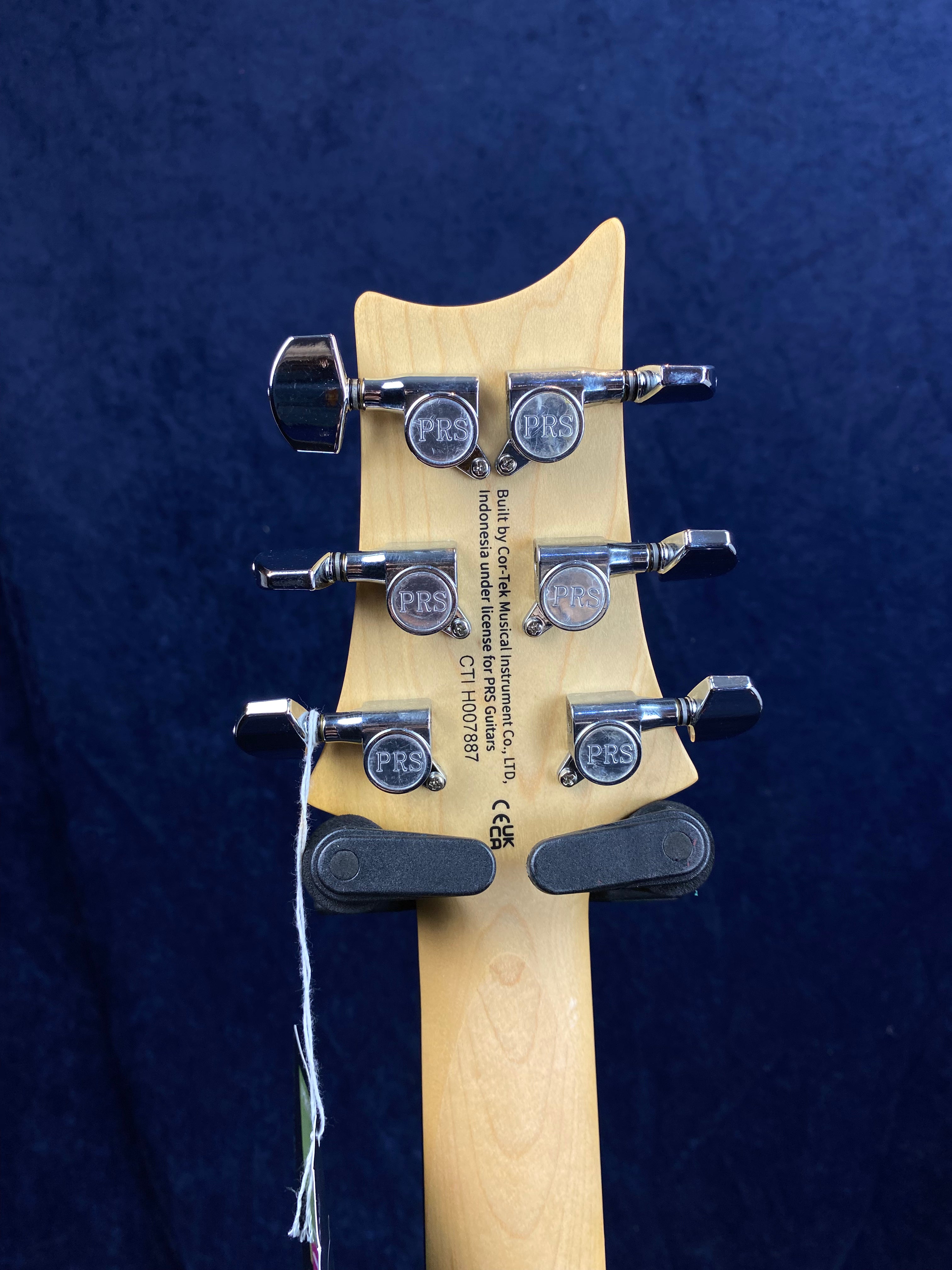 Back of a PRS electric guitar headstock showing four chrome tuners with "PRS" logos, a serial number, and manufacturer info printed on the wood.