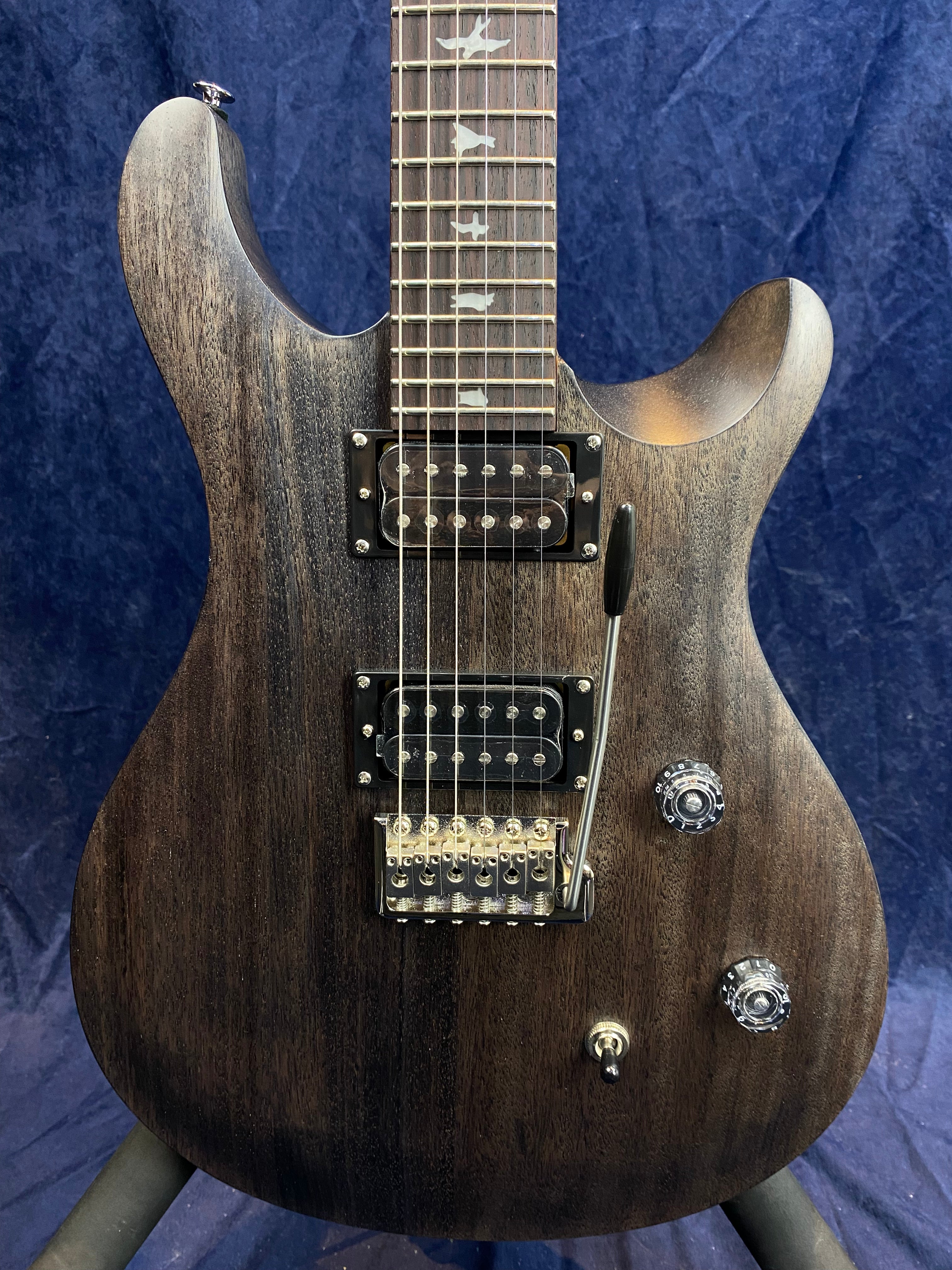 Matte dark brown electric guitar with two humbucker pickups, a tremolo bridge, two clear control knobs, a toggle switch, and bird inlays on the fretboard.
