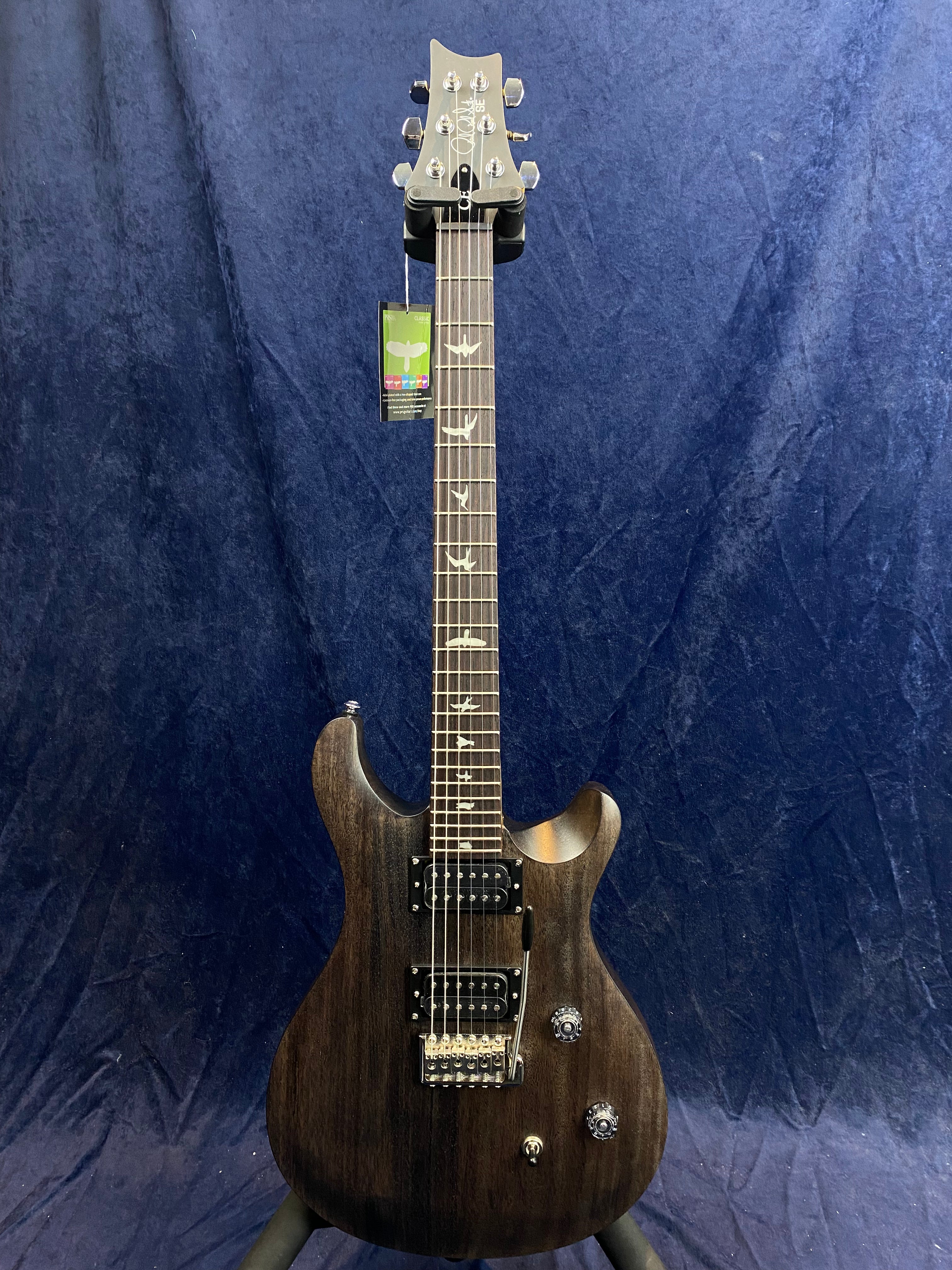 Dark wood electric guitar with two humbucker pickups, bird inlays on the fretboard, and chrome hardware, displayed upright against a navy blue background.