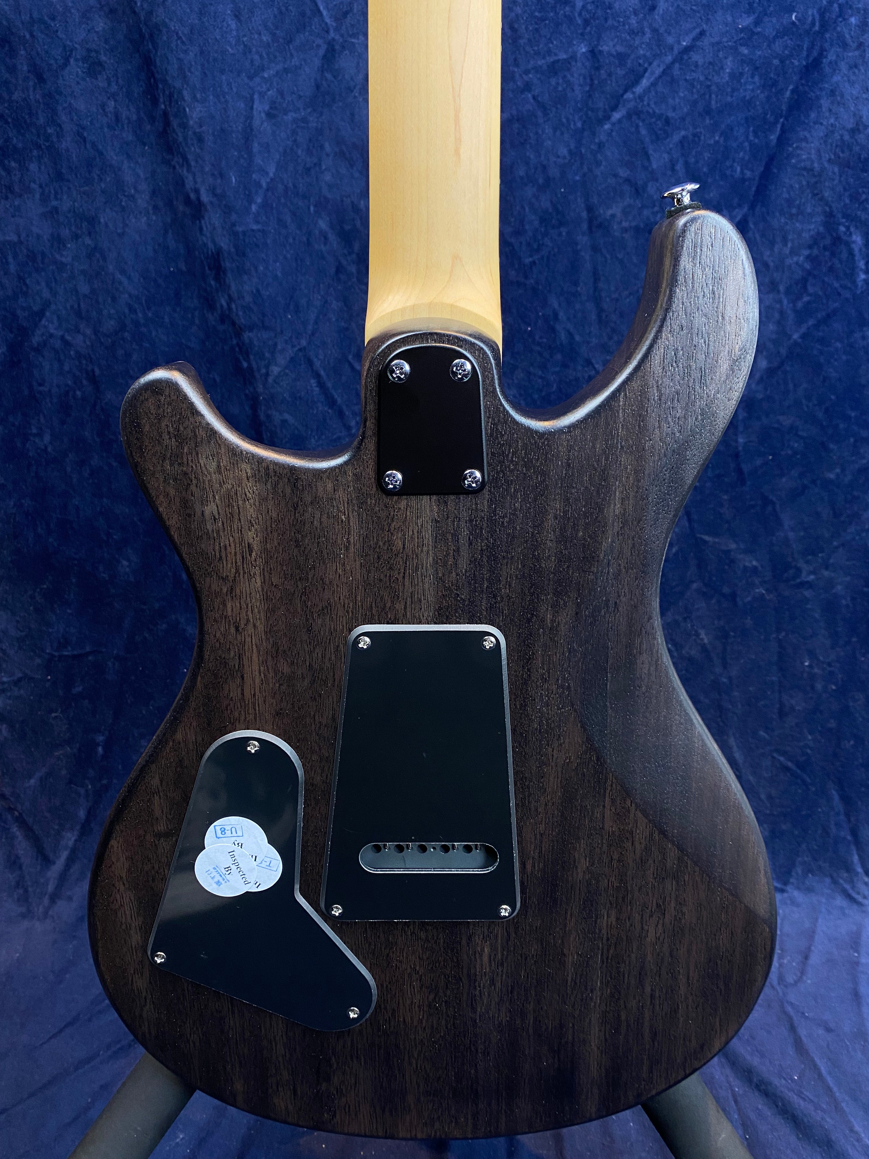 The back of a dark wood electric guitar body with a light maple neck, showing two black plastic cavity covers attached with screws.