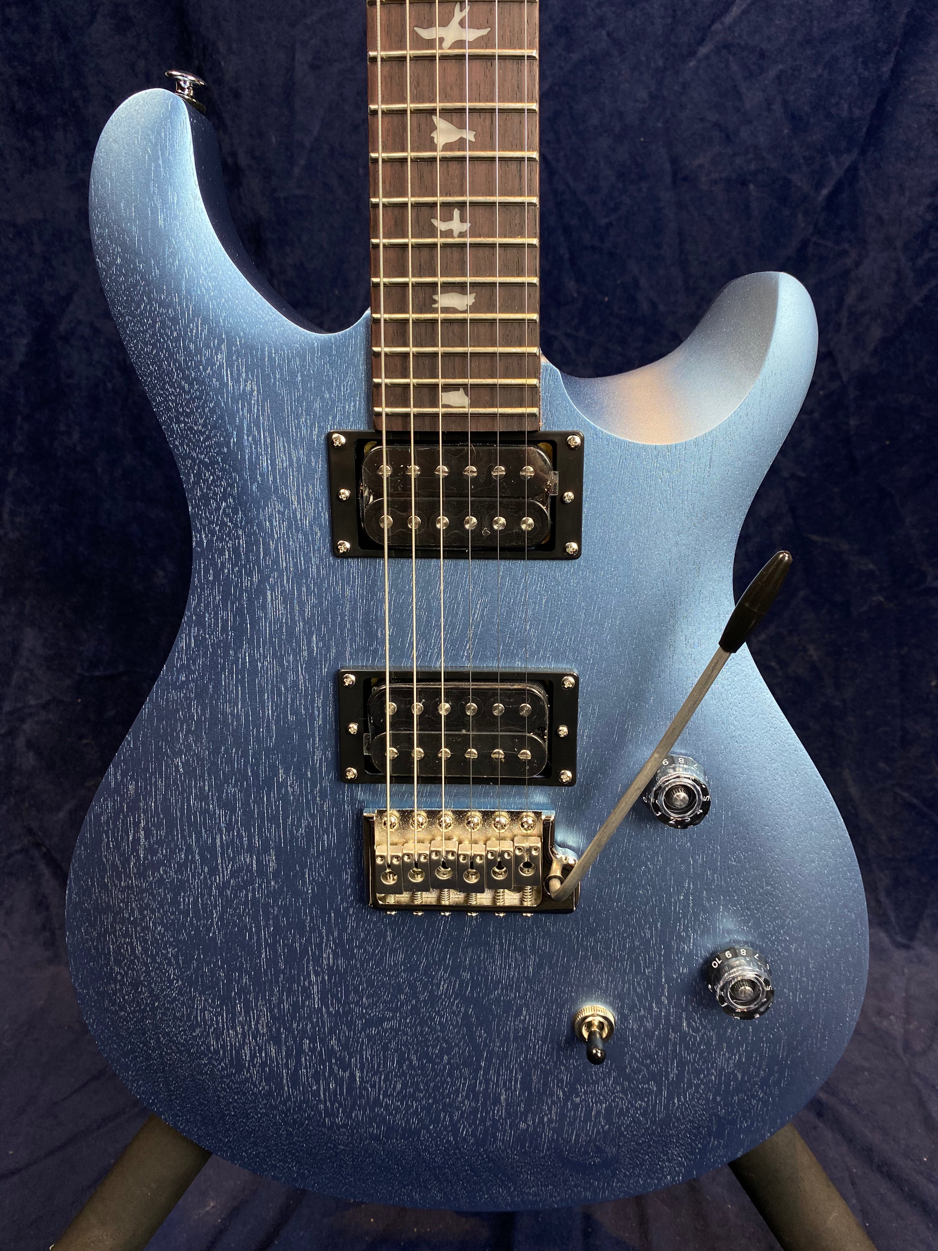 Blue electric guitar with a textured finish, two humbucker pickups, three knobs, a pickup switch, and a tremolo arm; fretboard has bird inlays.